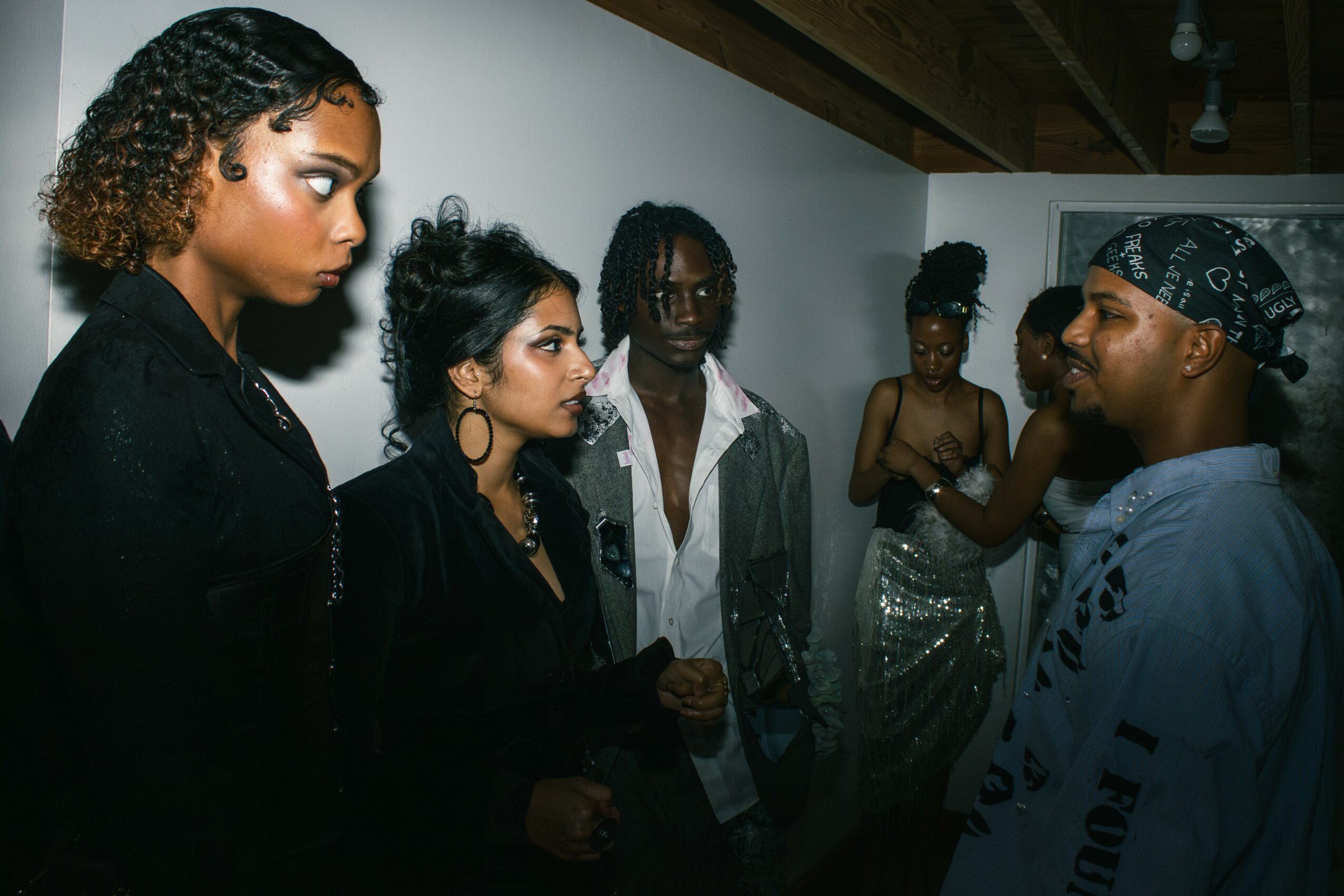 Group of six people engaged in conversation indoors, some wearing stylish clothing and accessories.