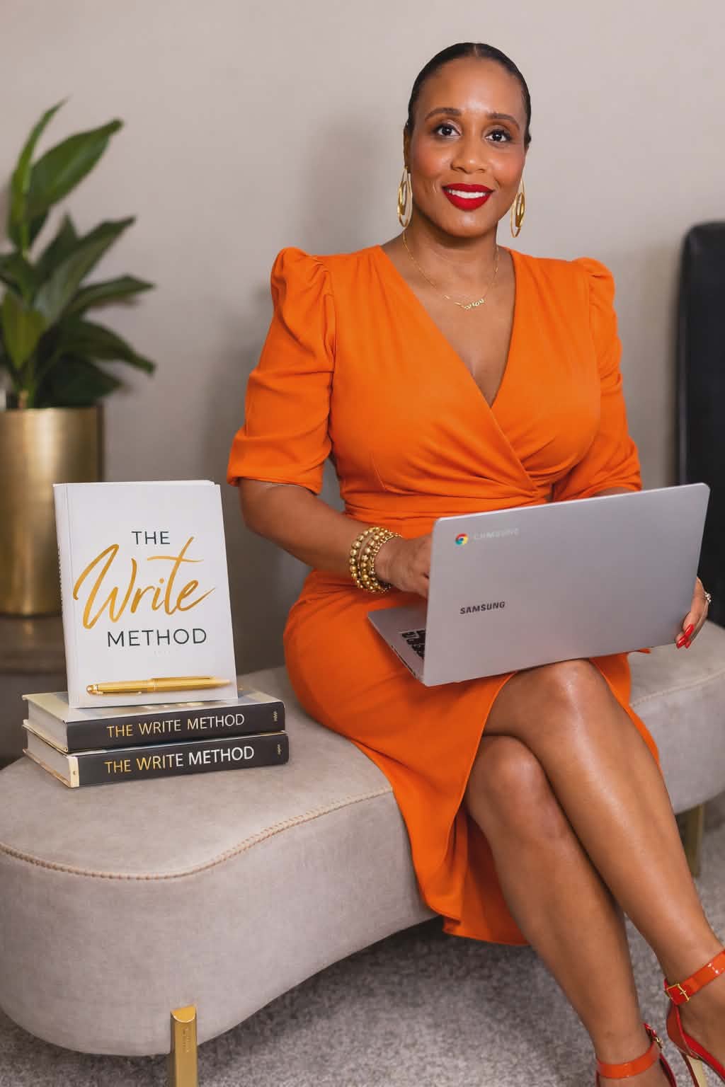 Woman in orange dress sitting on a sofa holding a laptop, with a plant and books nearby.