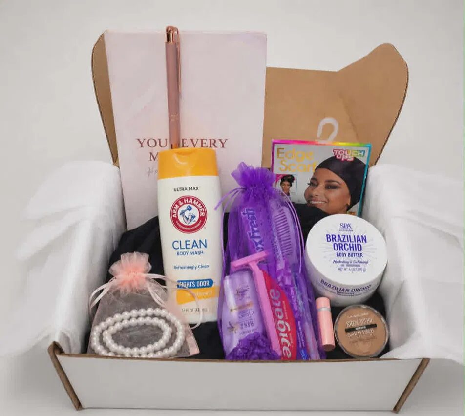 Open gift box with skincare, hairbrush, jewelry, and beauty products inside, on a white surface.
