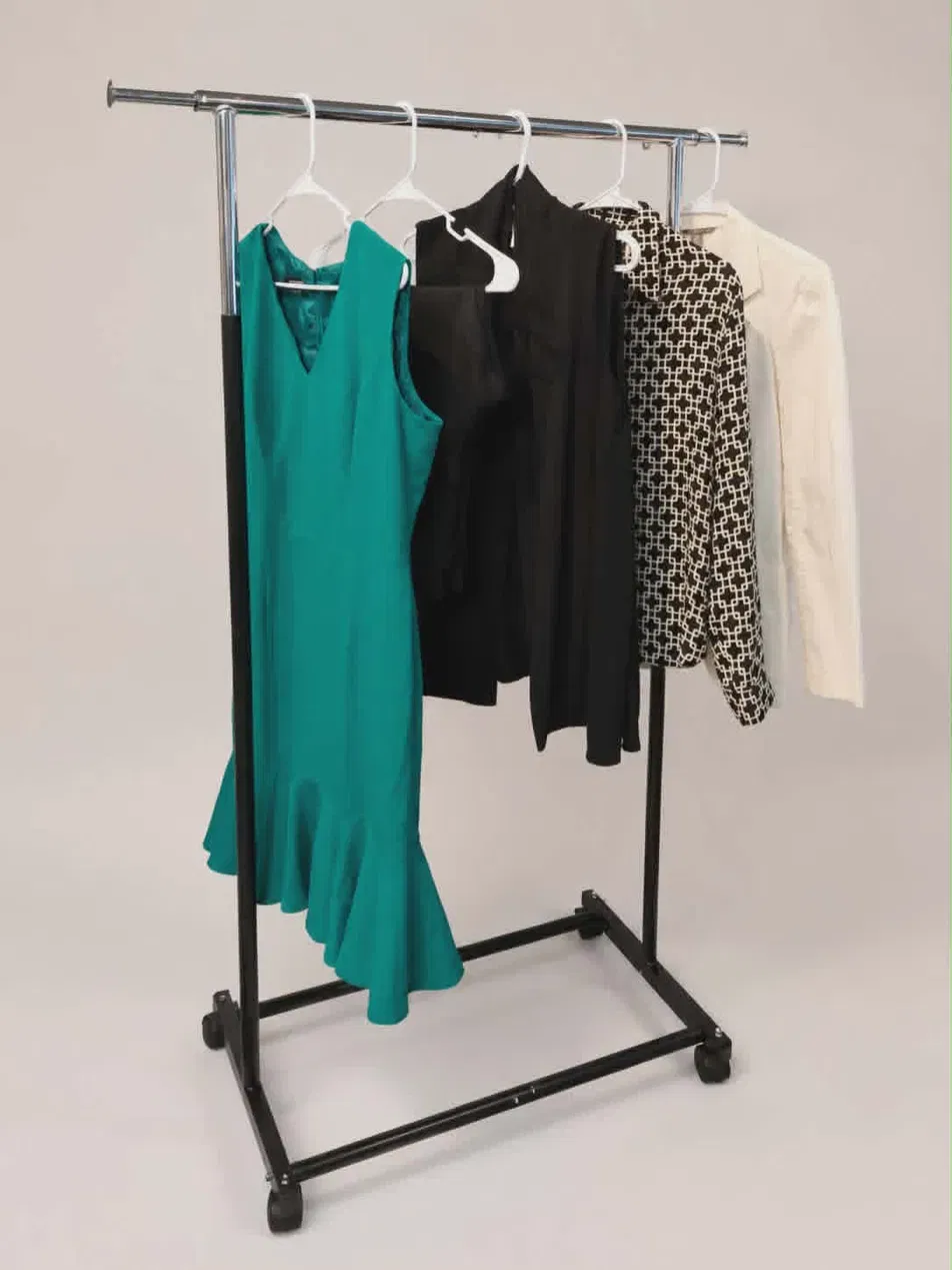 Clothing rack with five hanging garments, including a teal dress, black top, patterned blouse, and white shirt, against a plain background.