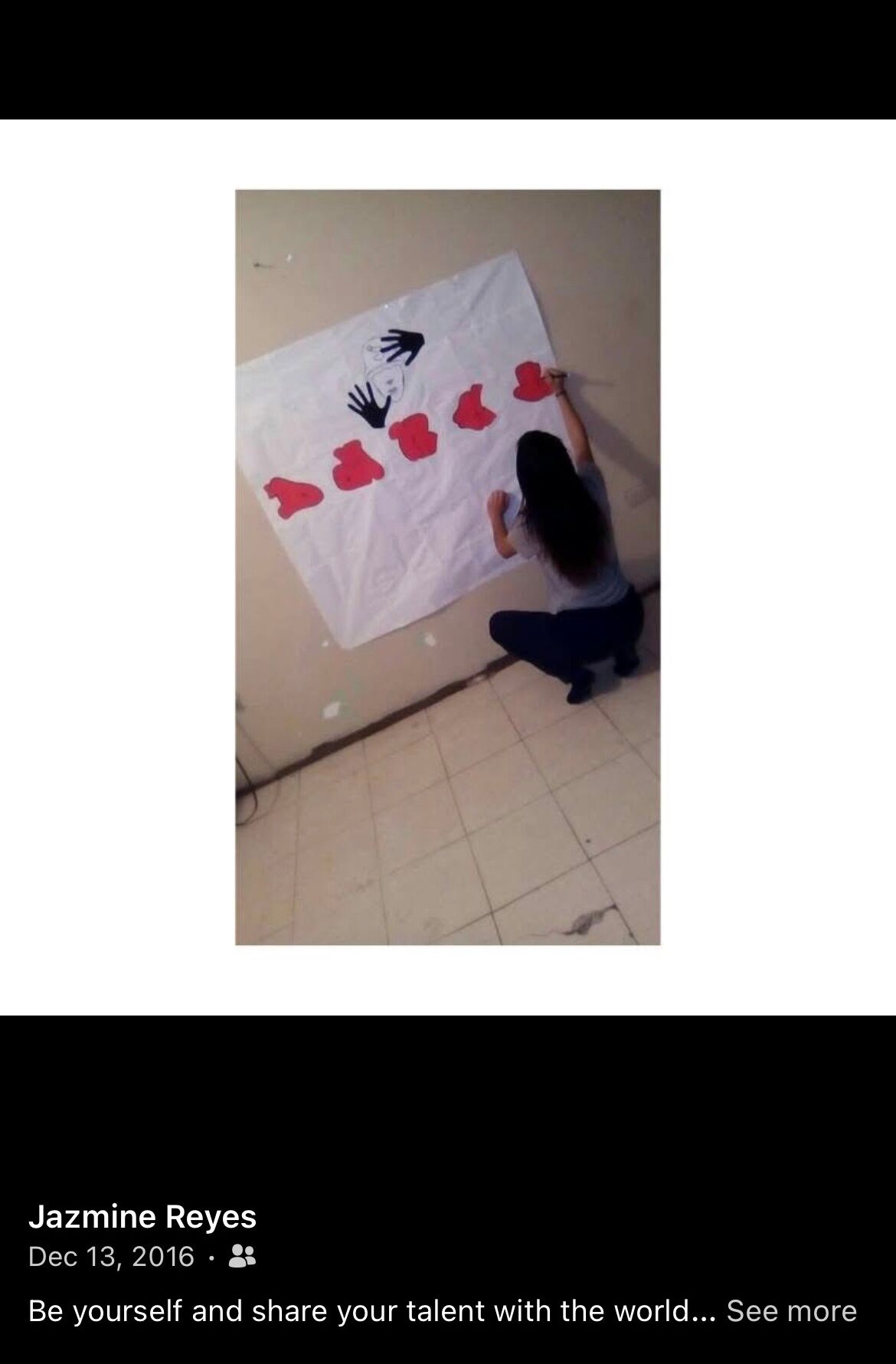 Person working on a large white paper with red and black shapes, on a tiled floor, viewed from above.