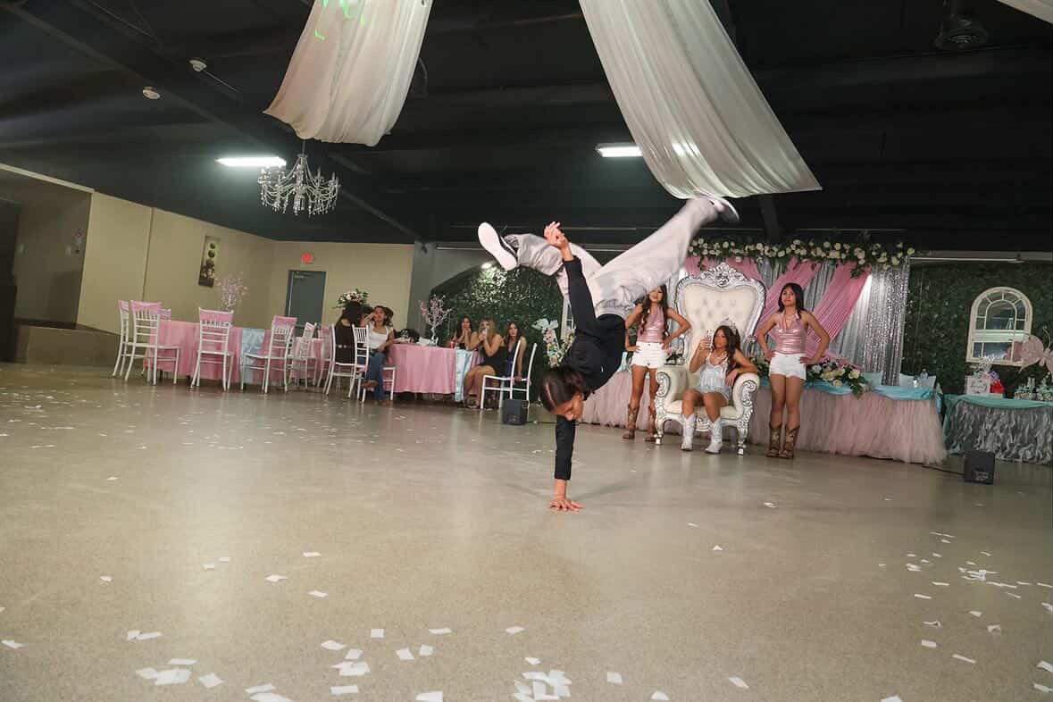 Person performing a handstand in a decorated event hall with pink and white tables and chairs, and guests watching.