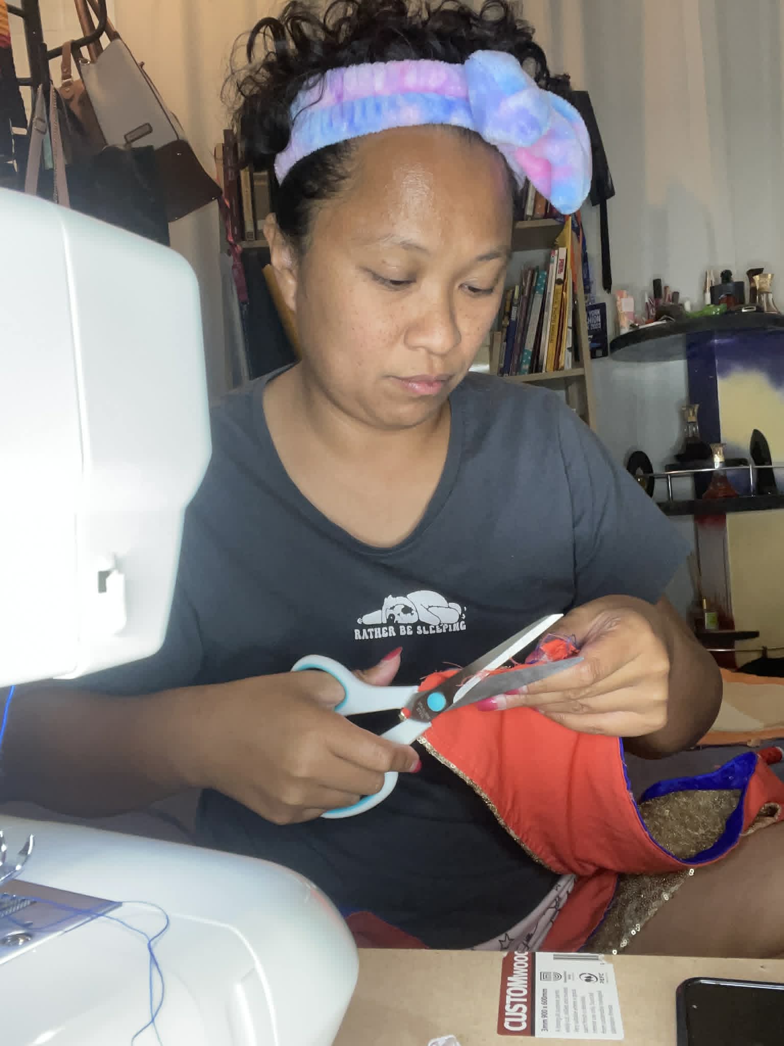 Woman with a colorful headband cutting fabric with scissors in a room with books and supplies