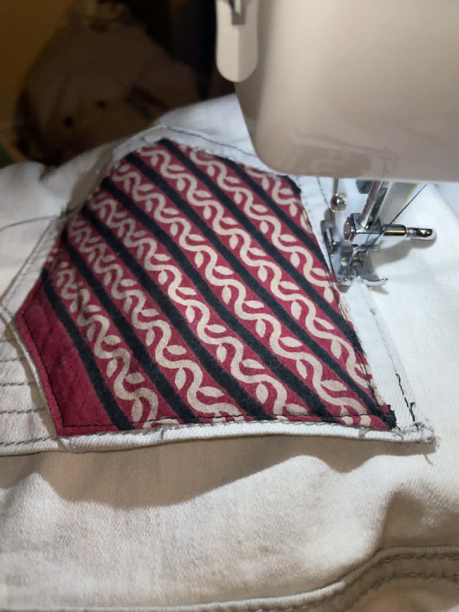 A sewing machine stitching a colorful fabric with red, black, and beige patterns, on a white surface.