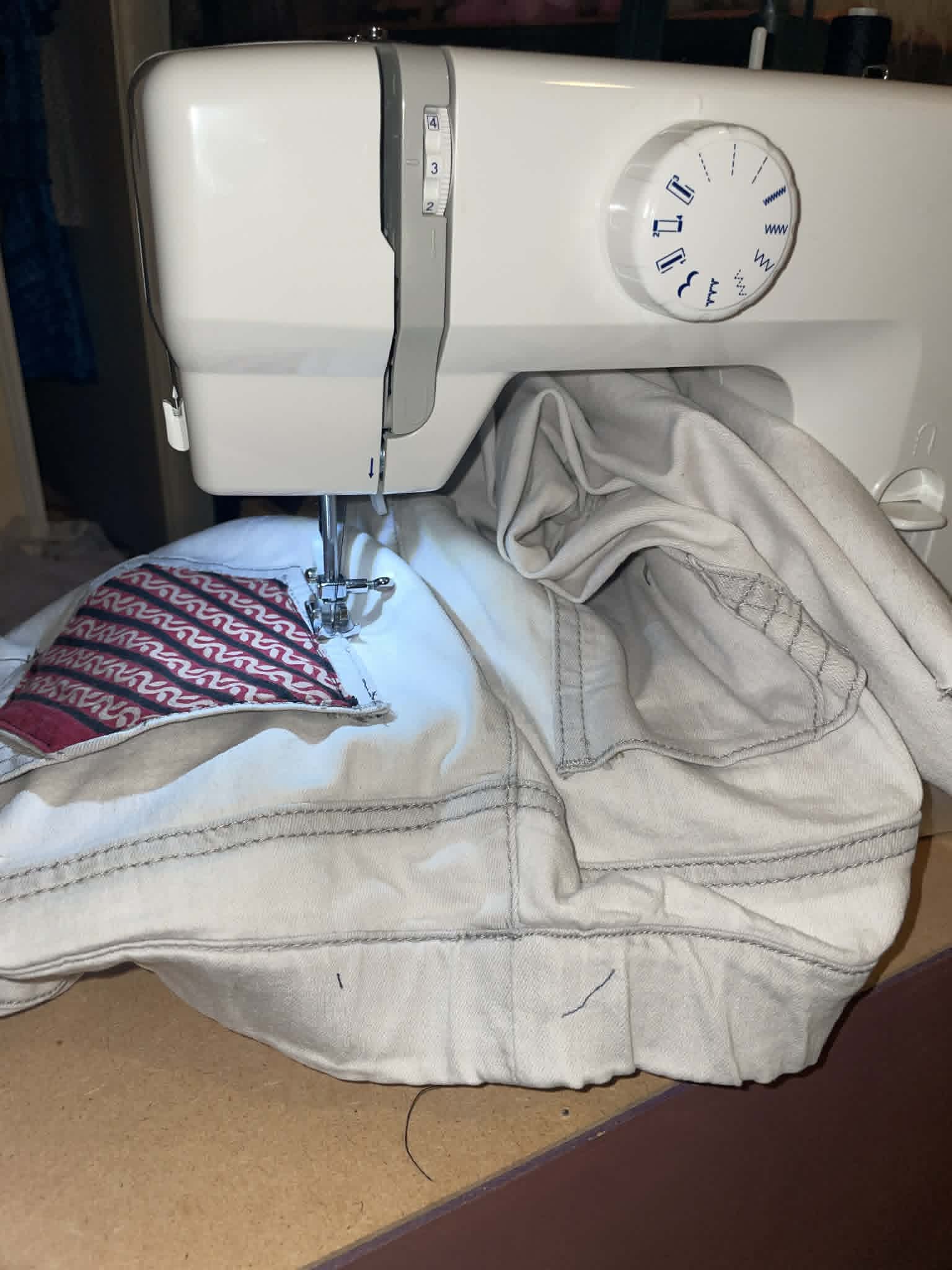 Sewing machine stitching fabric with denim and patterned material, fabric draped over machine, close-up view.