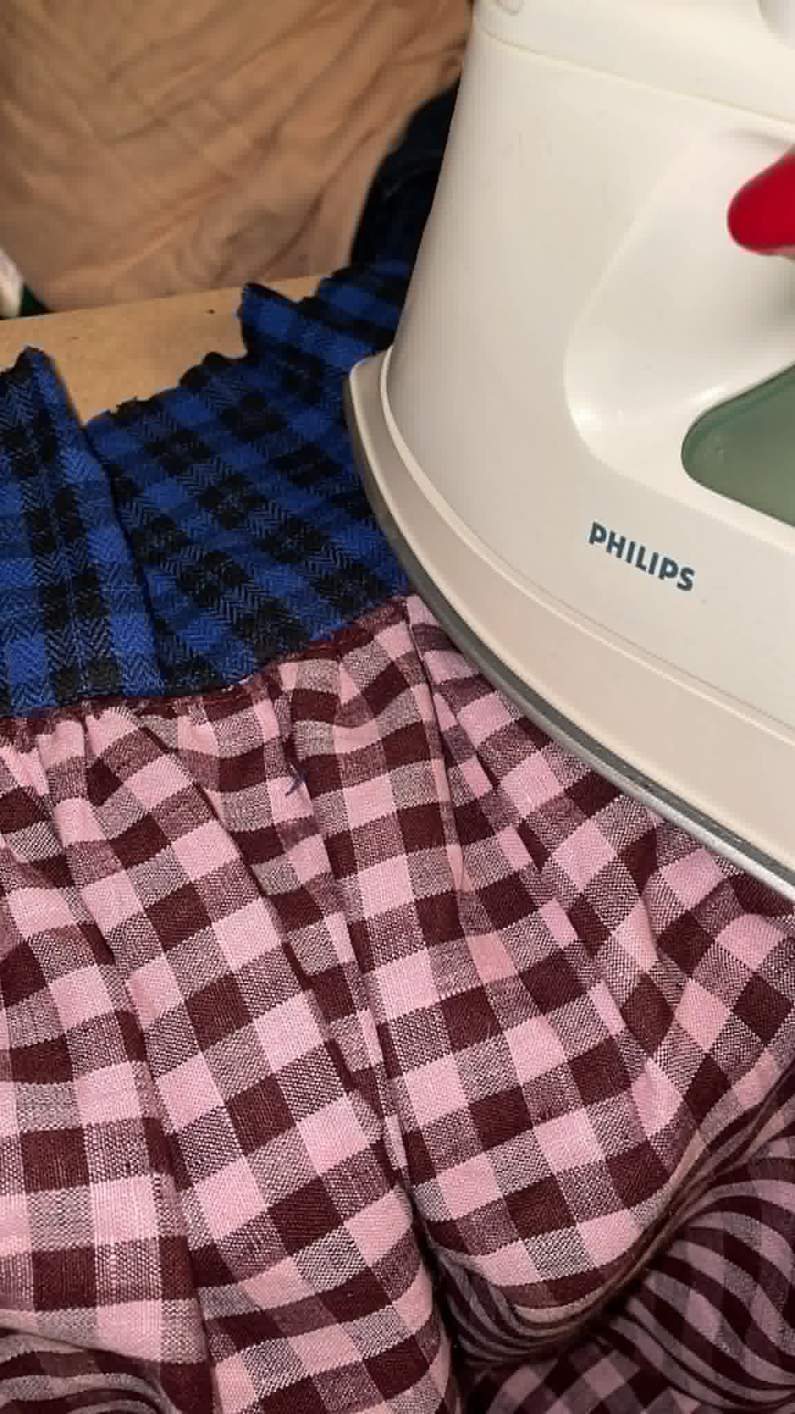 Close-up of a person wearing pink checkered pants and a blue checkered shirt, with a white Philips iron nearby.