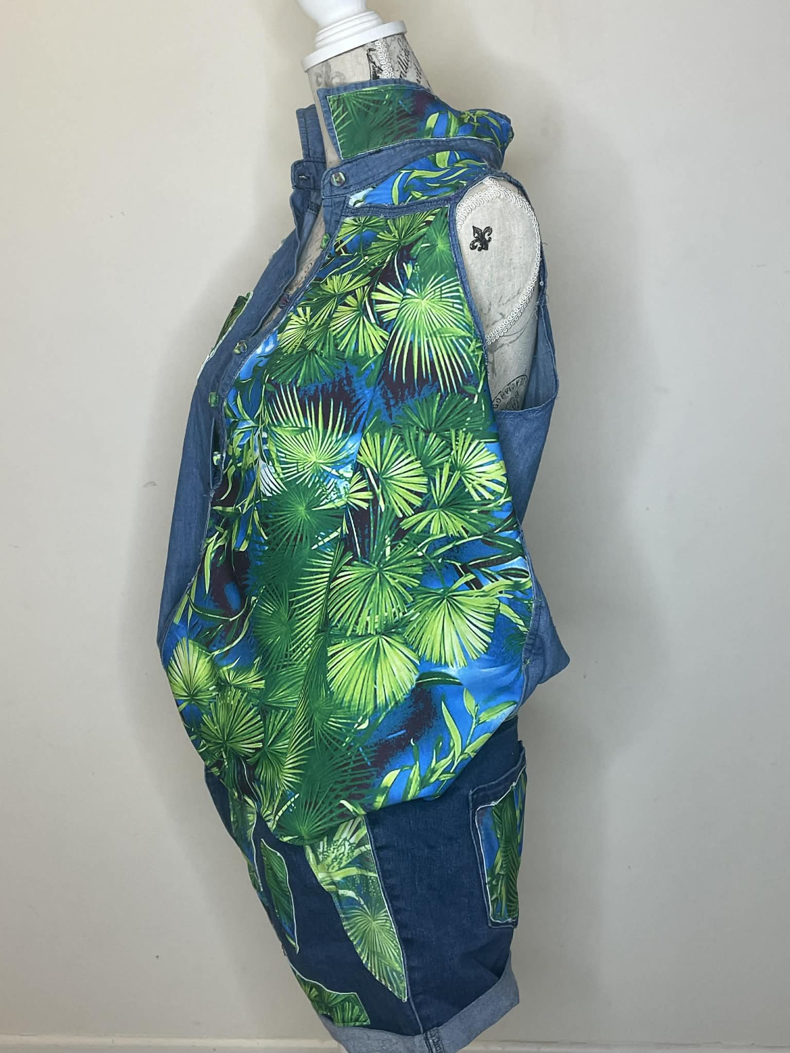 A backpack with a green and blue tropical leaf pattern, containing a water bottle, against a plain wall.
