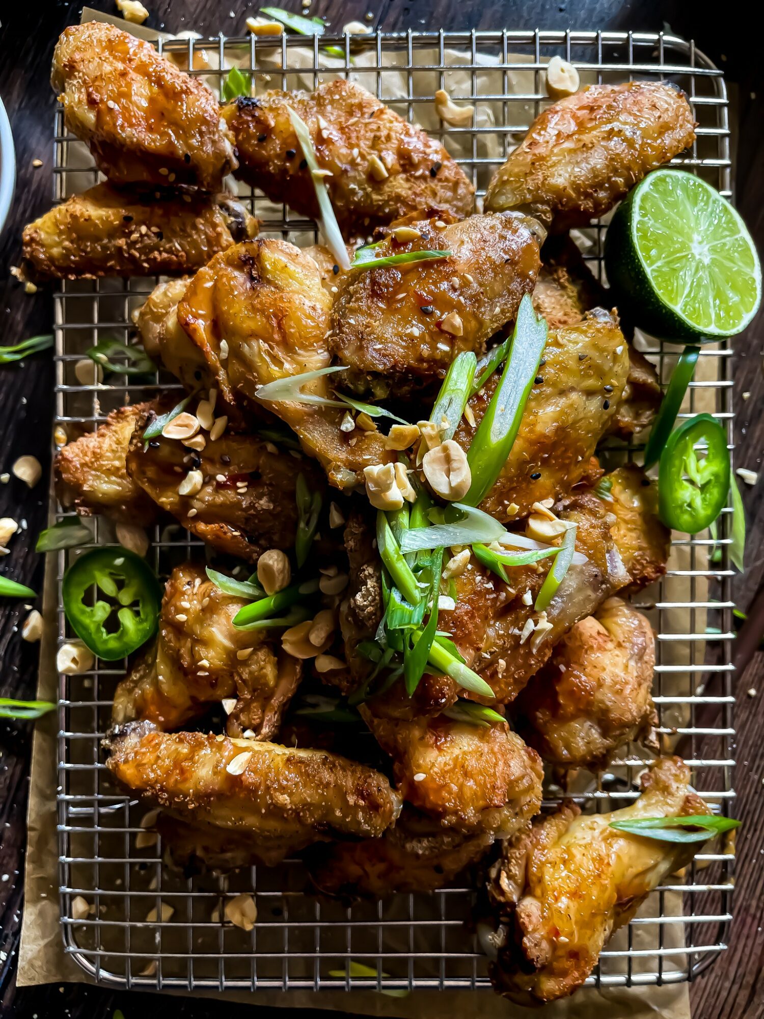Fried chicken wings garnished with sliced green chili, green onion, and lime on a wire rack.