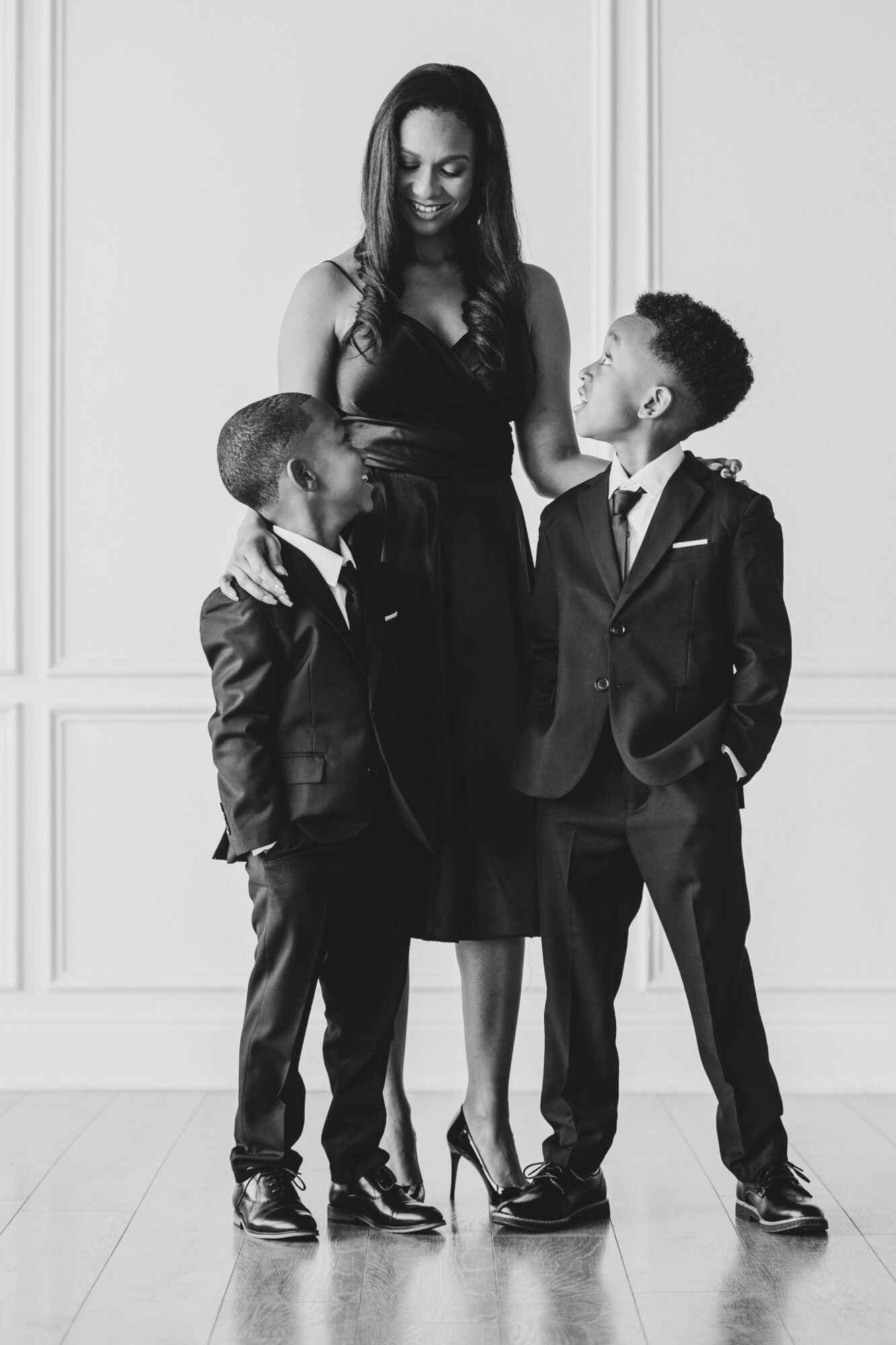 Woman with two young boys in formal suits standing together indoors, woman smiling at boys, black and white photo.