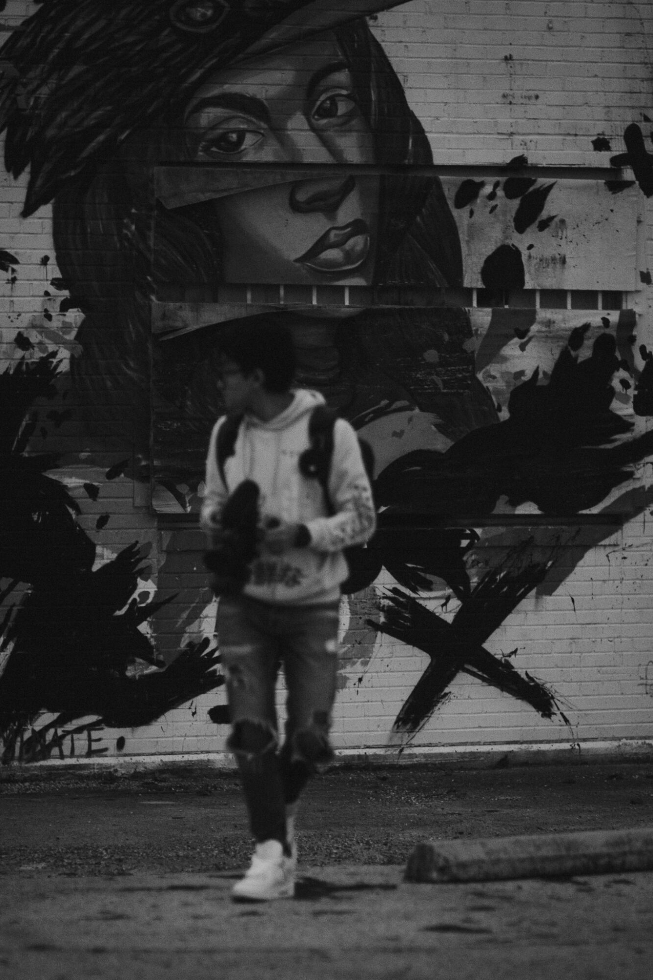 Person walking in front of a large mural of a woman's face on a brick wall, black and white.