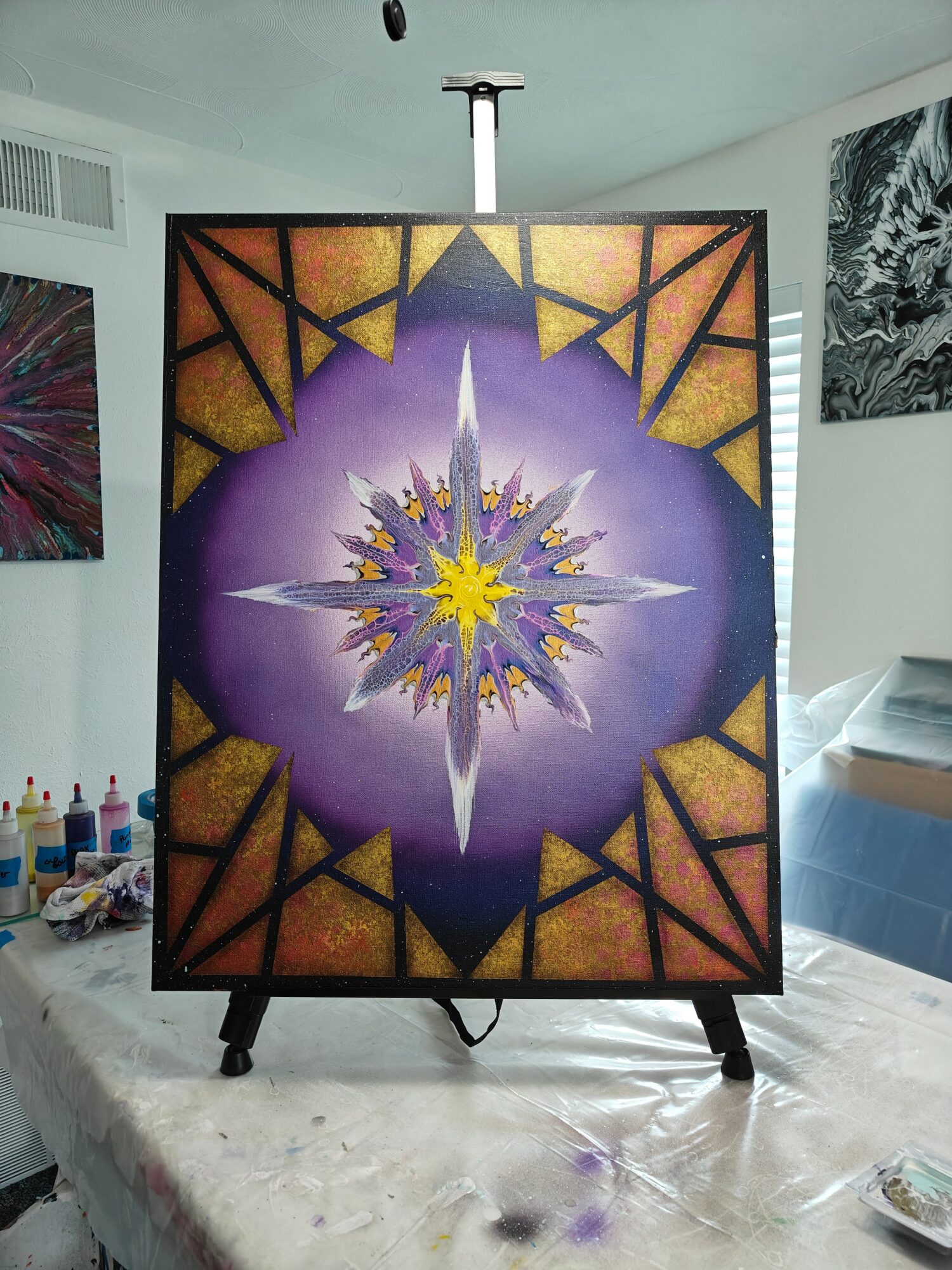 Colorful geometric and symmetrical design with purple, yellow, and orange elements on a framed artwork, standing on a table.