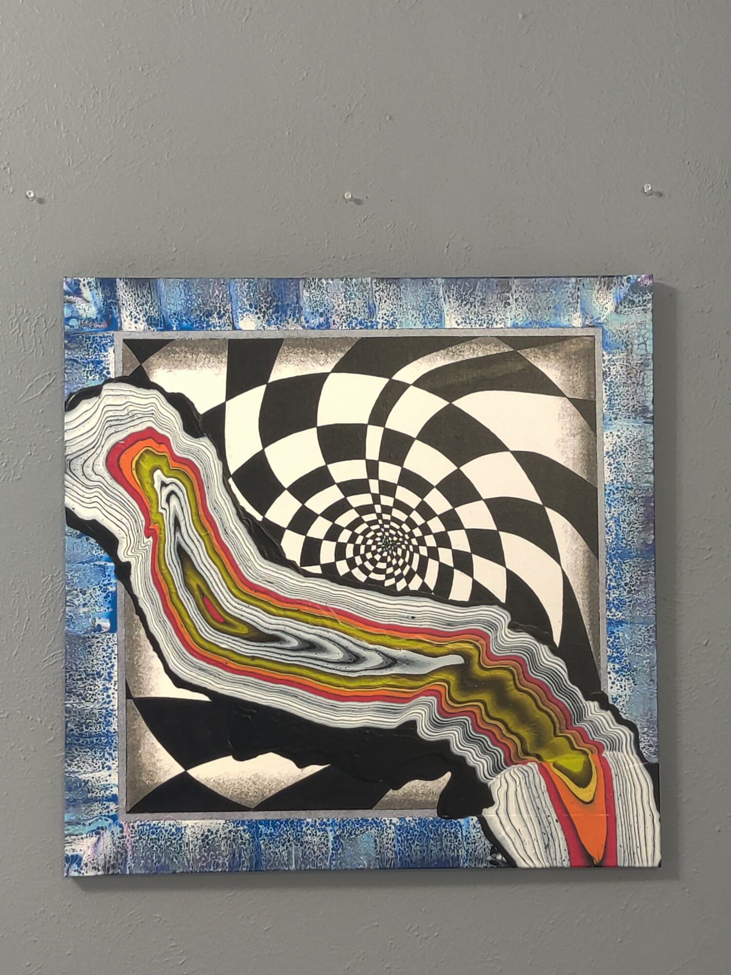 Abstract artwork with black and white checkered spiral and colorful wavy lines, framed on a gray wall.