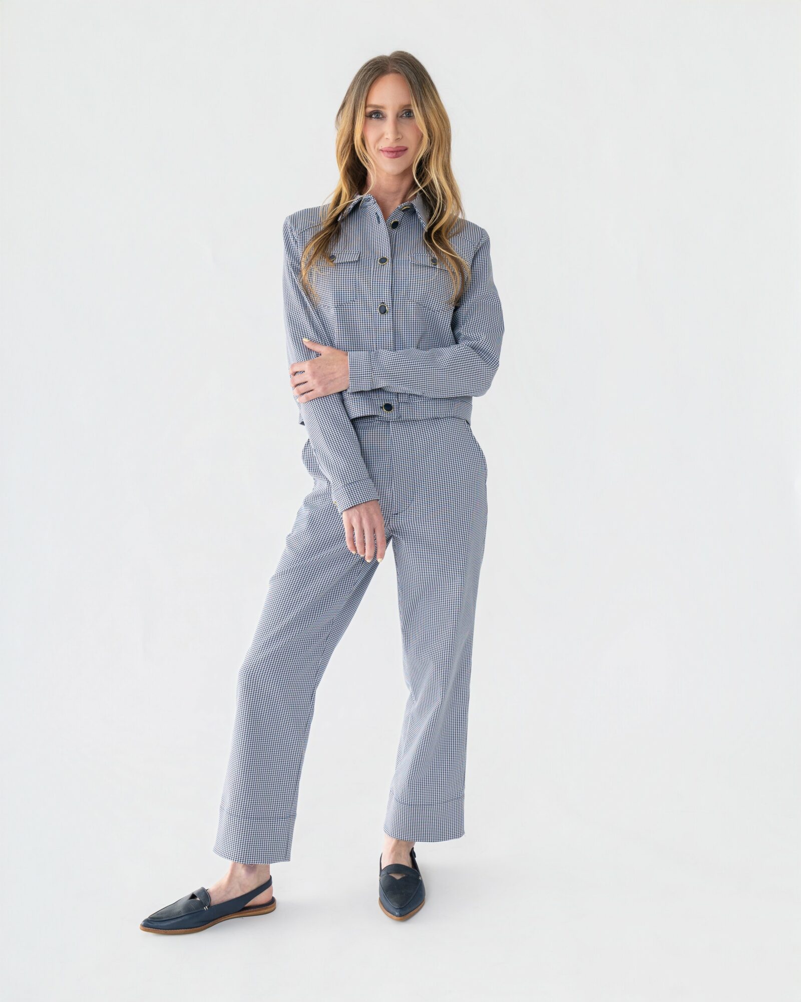Woman in striped shirt and pants standing with arms crossed, smiling, against a plain white background.