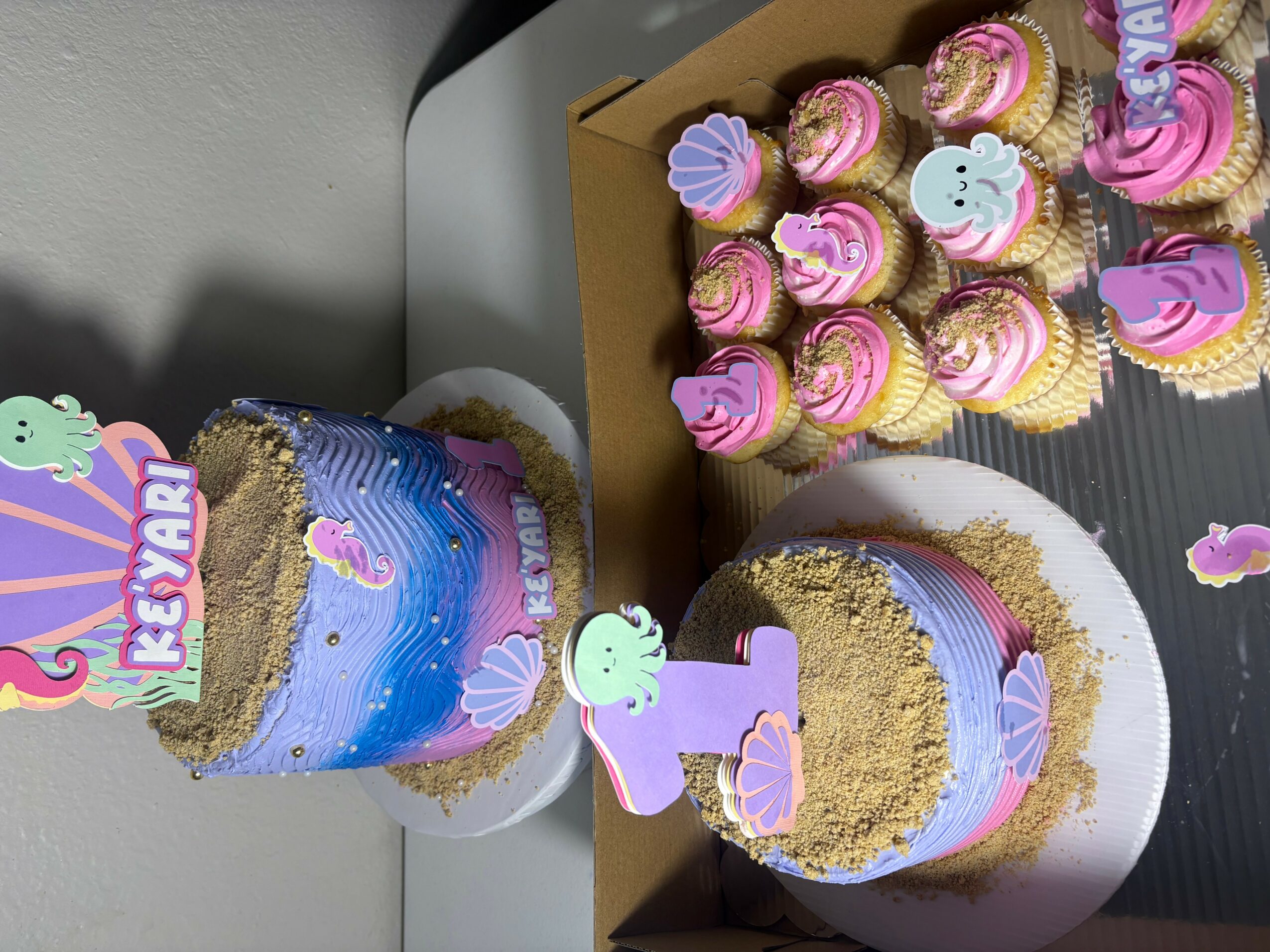 Celebration with cupcakes and a colorful cake, decorated with pastel colors and themed toppers, on a table.