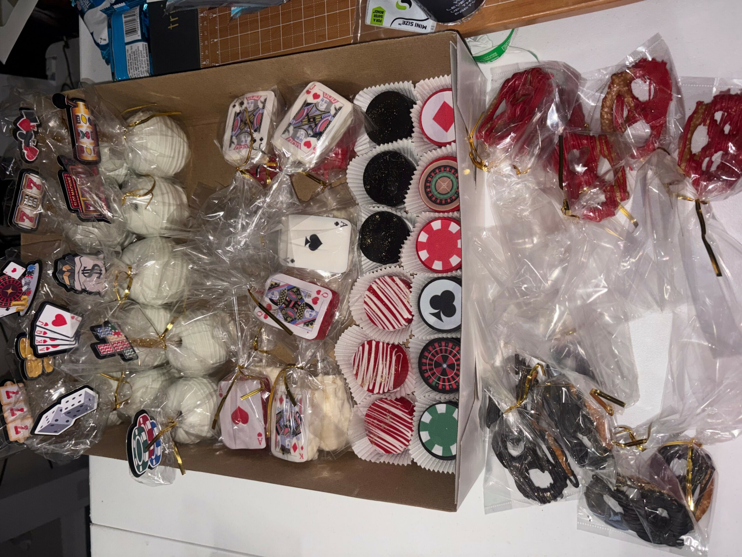 Box filled with decorated cupcakes and treats, some wrapped in plastic, with additional treats on the side.