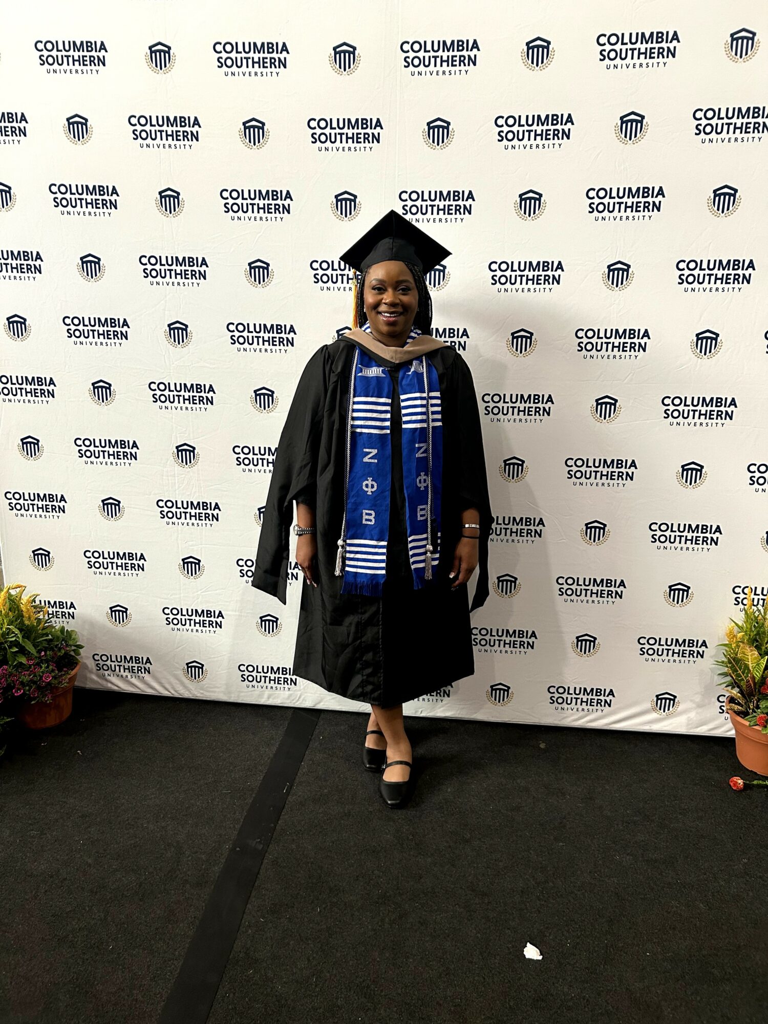 Young woman in graduation gown and stole standing in front of a Columbia Southern University backdrop, smiling.