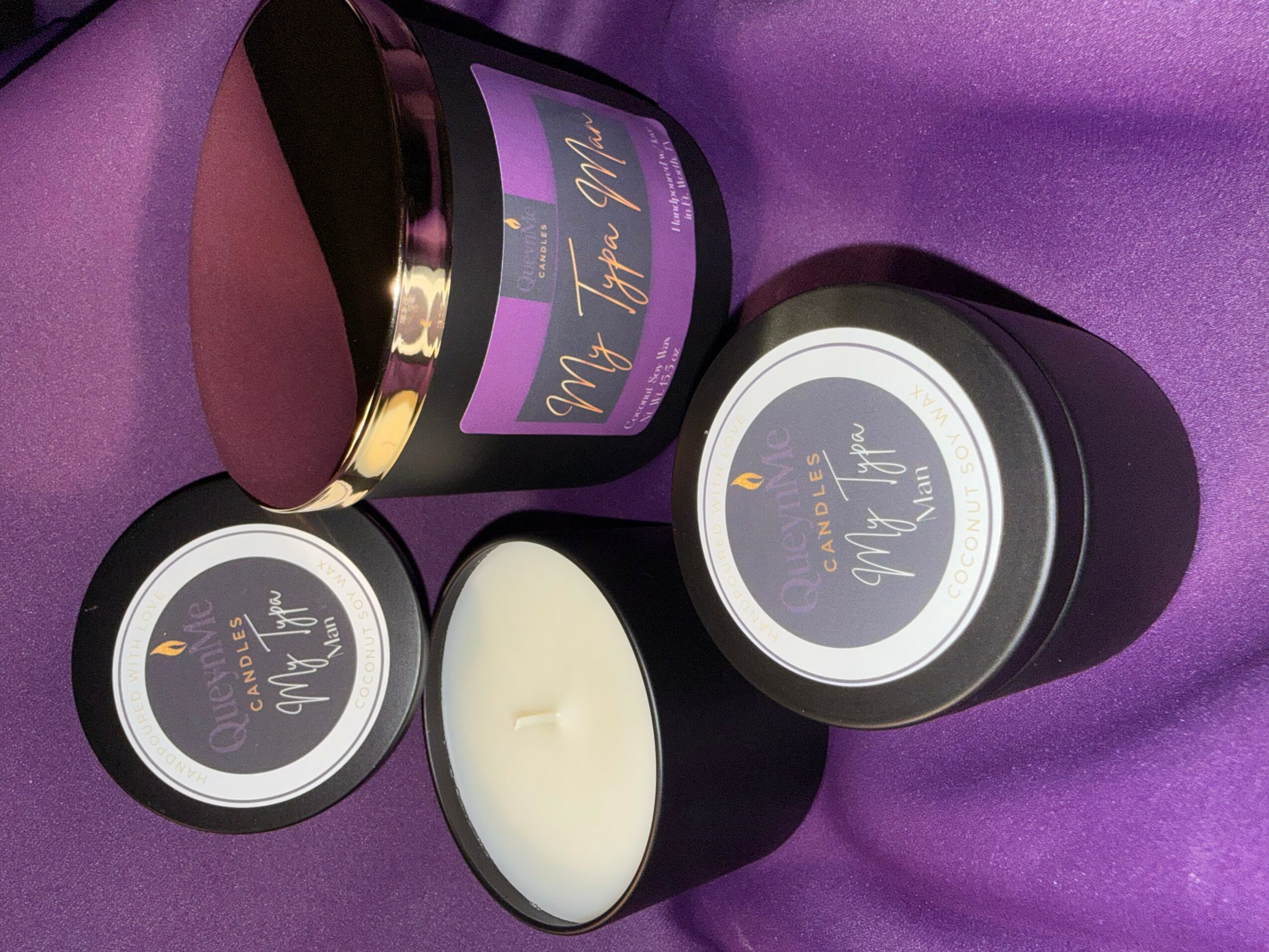 Three black containers with purple labels and a white candle on purple fabric background.