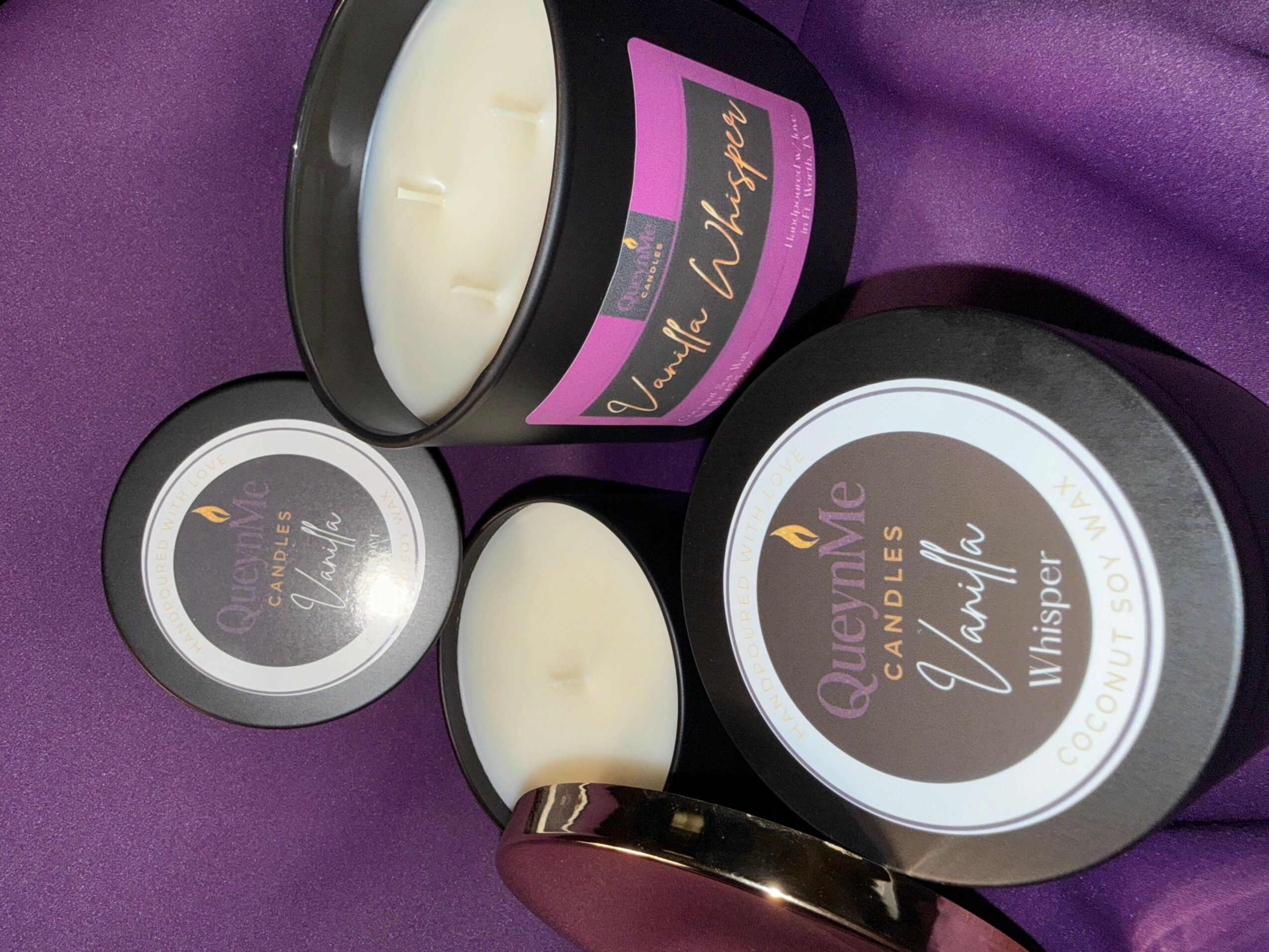 Open candle container with white wax, purple label, and lid nearby on purple fabric.