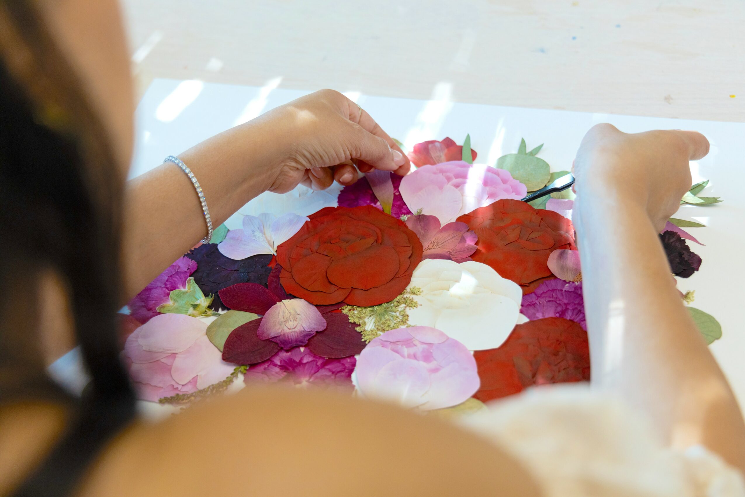 Person arranging colorful flower petals on a surface, with hands visible and a bracelet on the left wrist.