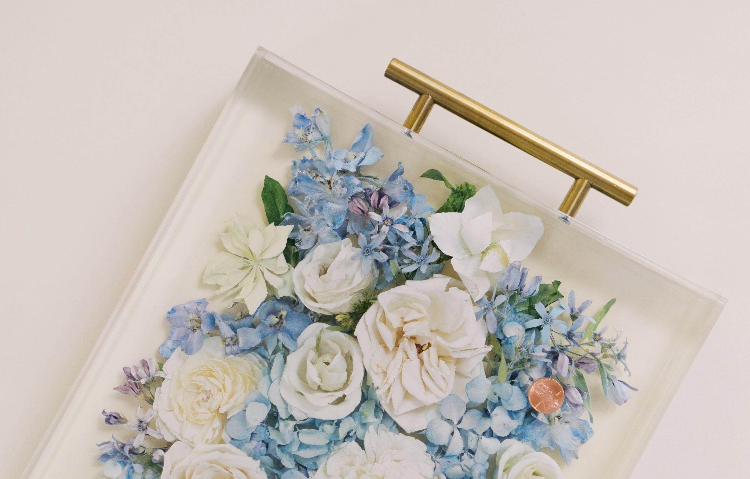 Close-up of a floral arrangement with white and blue flowers, and a gold handle above, on a white background.