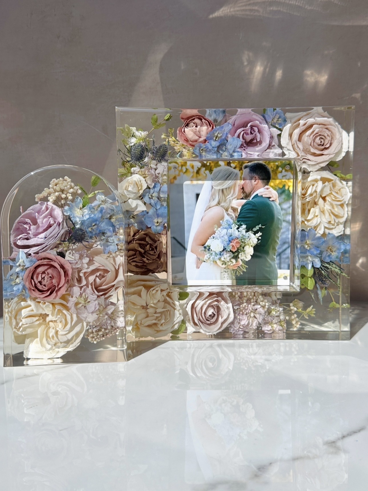 Decorative floral arrangement with a framed wedding photo of a couple, featuring roses and other flowers in pastel colors.