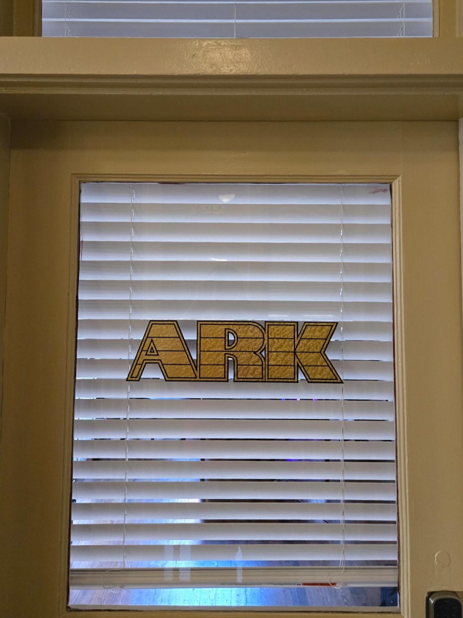 Window with closed blinds and a sign that reads 'ARK' in gold letters.