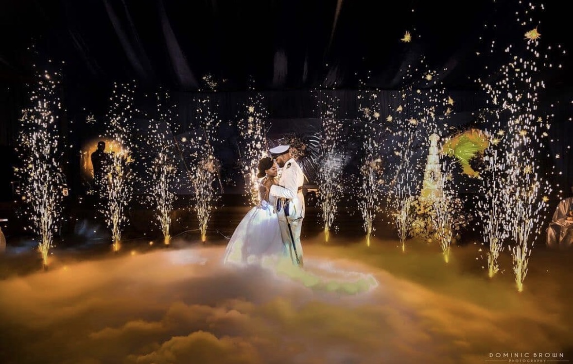 Couple dancing on stage with fireworks and fog, illuminated by bright lights, celebrating a special event.