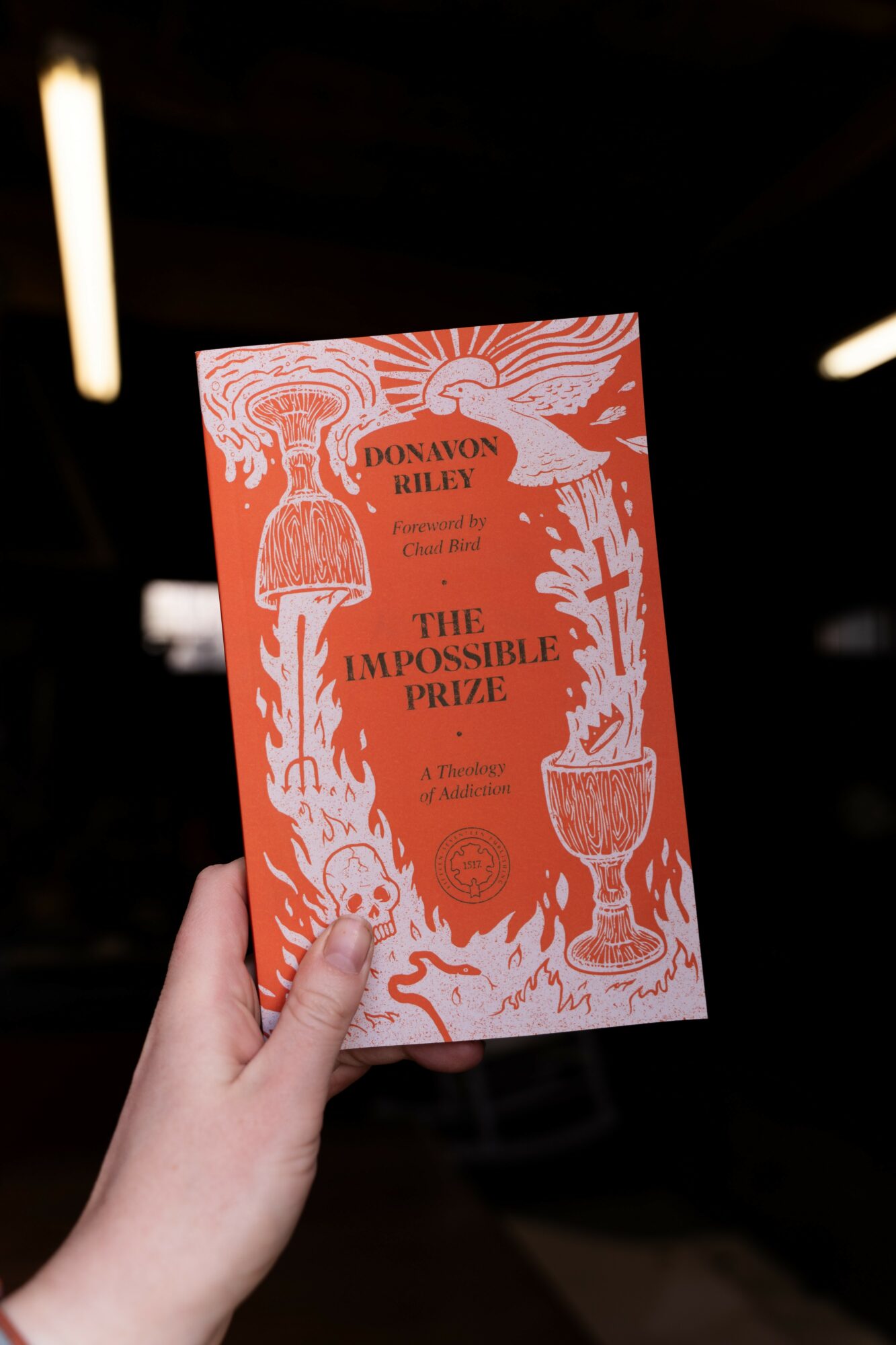 Hand holding a book titled 'The Impossible Prize' with orange and white illustrations, against a dark background.