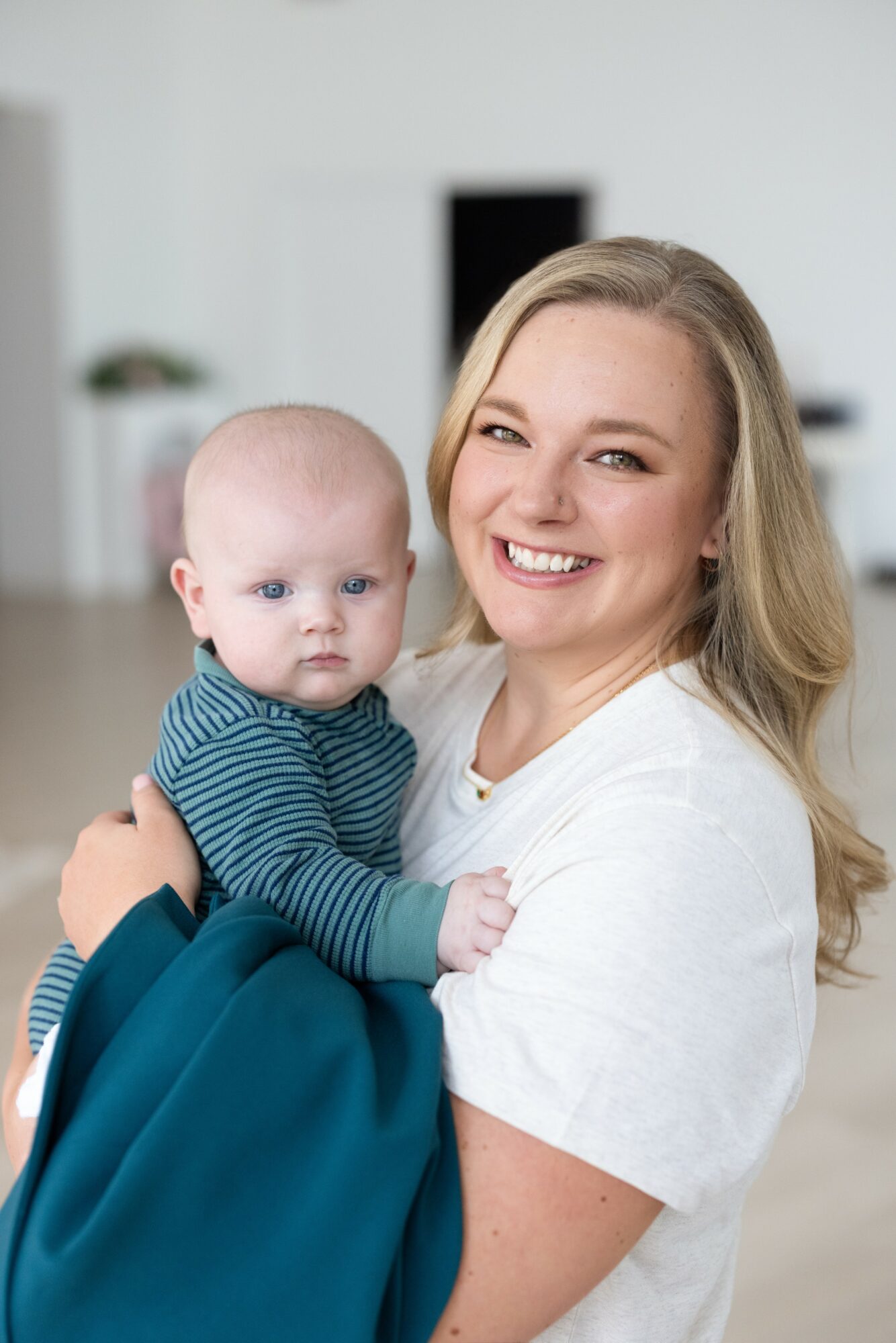 Smiling woman holding a baby with a striped shirt in a bright room.