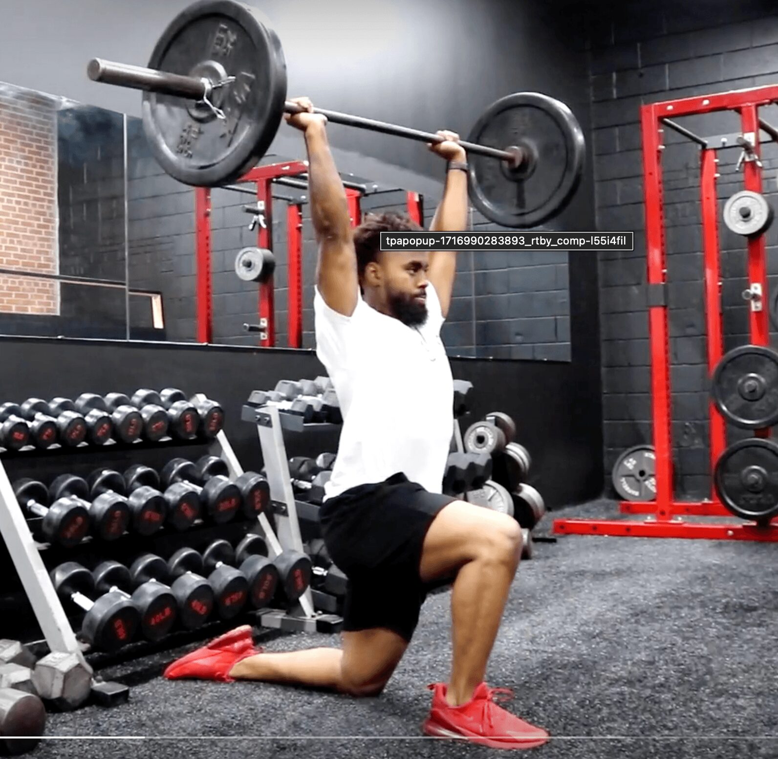 Man performing a shoulder press exercise in a gym, kneeling on one knee with weights overhead.