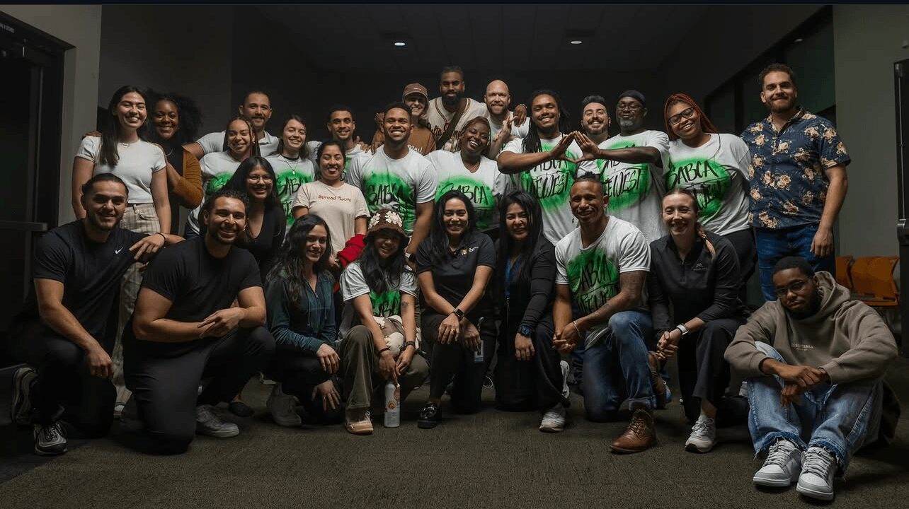Group of people posing indoors, some wearing green and white shirts, smiling and sitting or standing together.