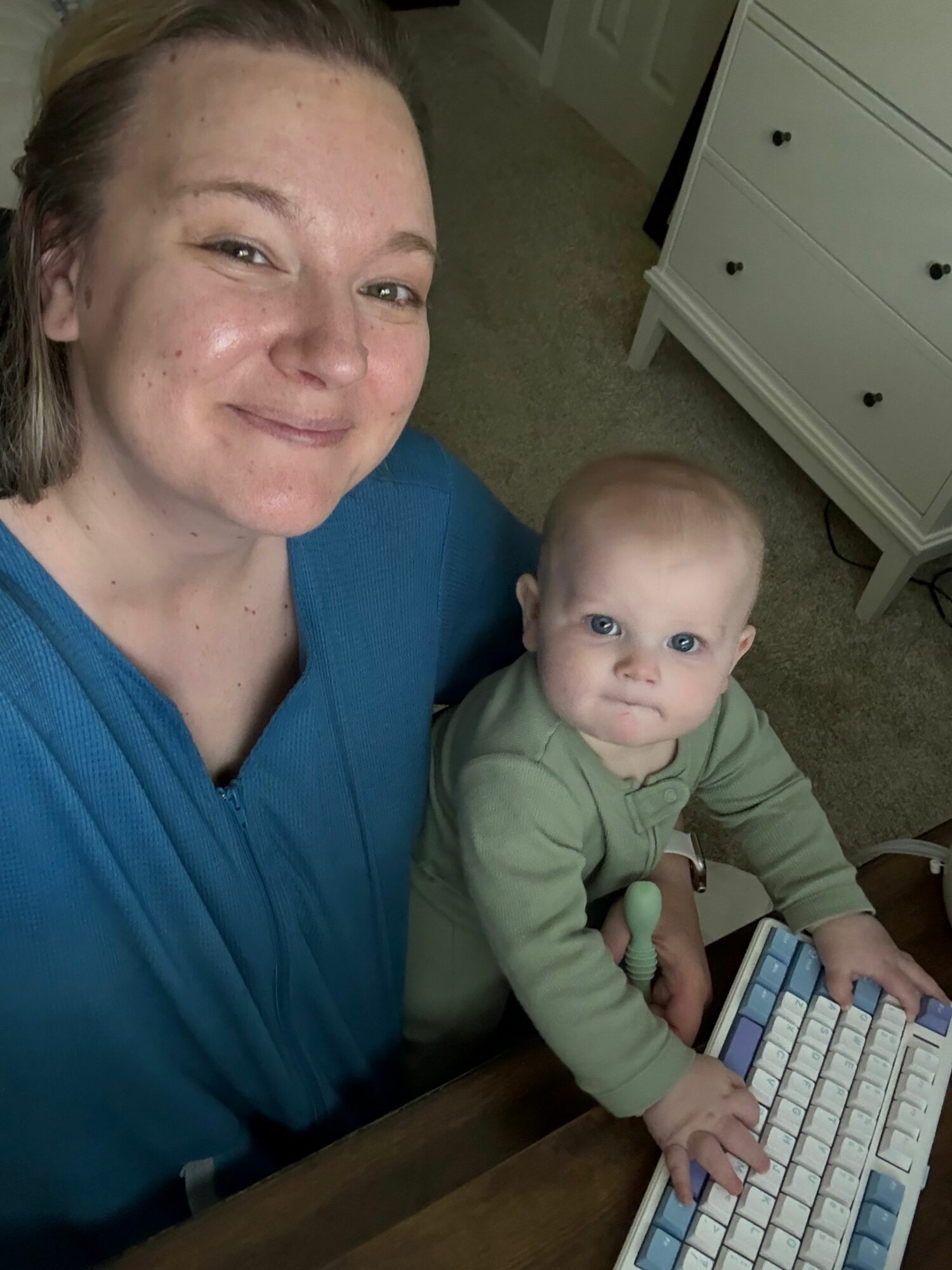 Woman and child sitting at a desk with a keyboard, looking at the camera, in a room with a white dresser.
