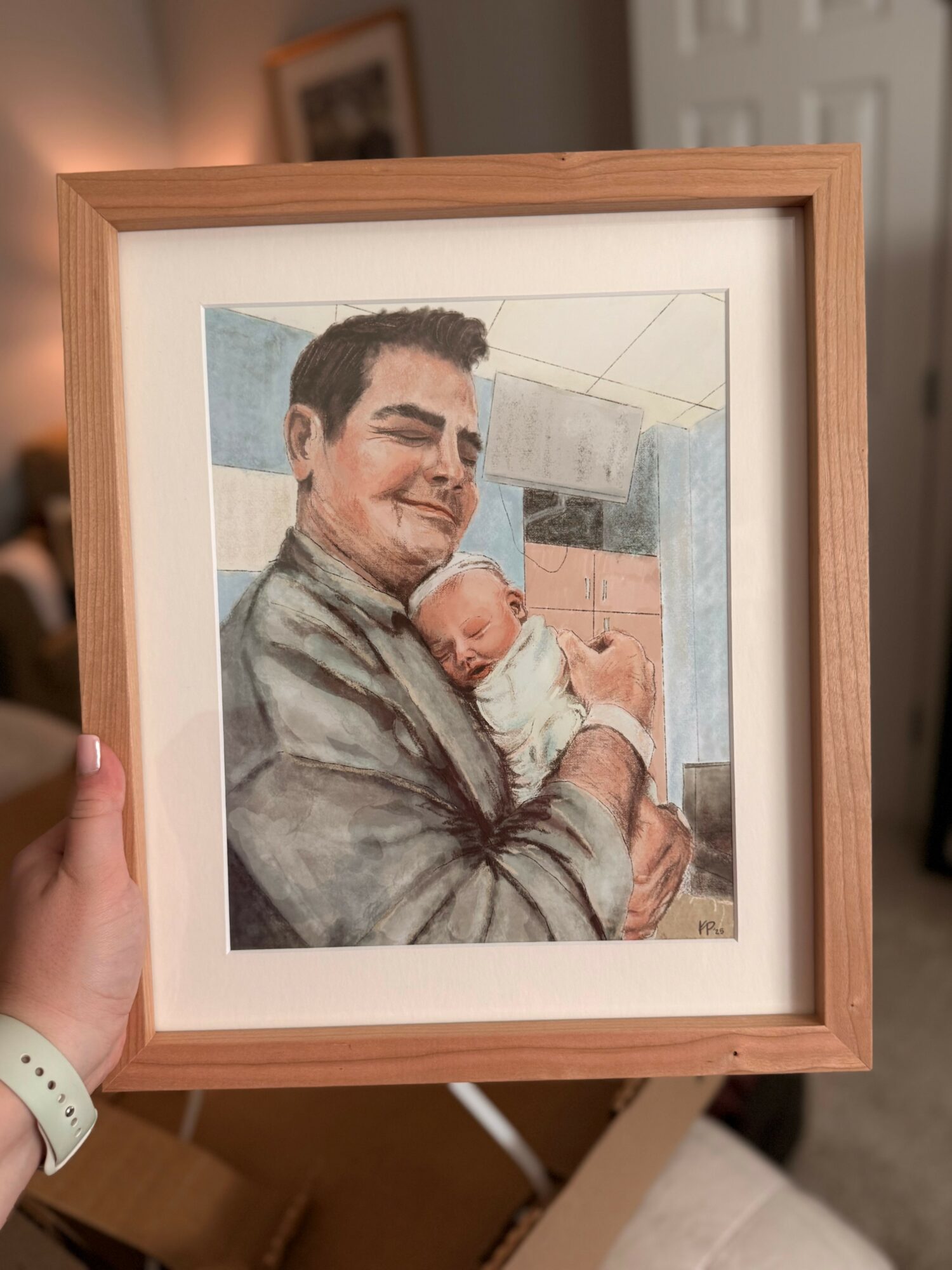 Framed watercolor painting of a man holding a baby, smiling, indoors with a blurred background.