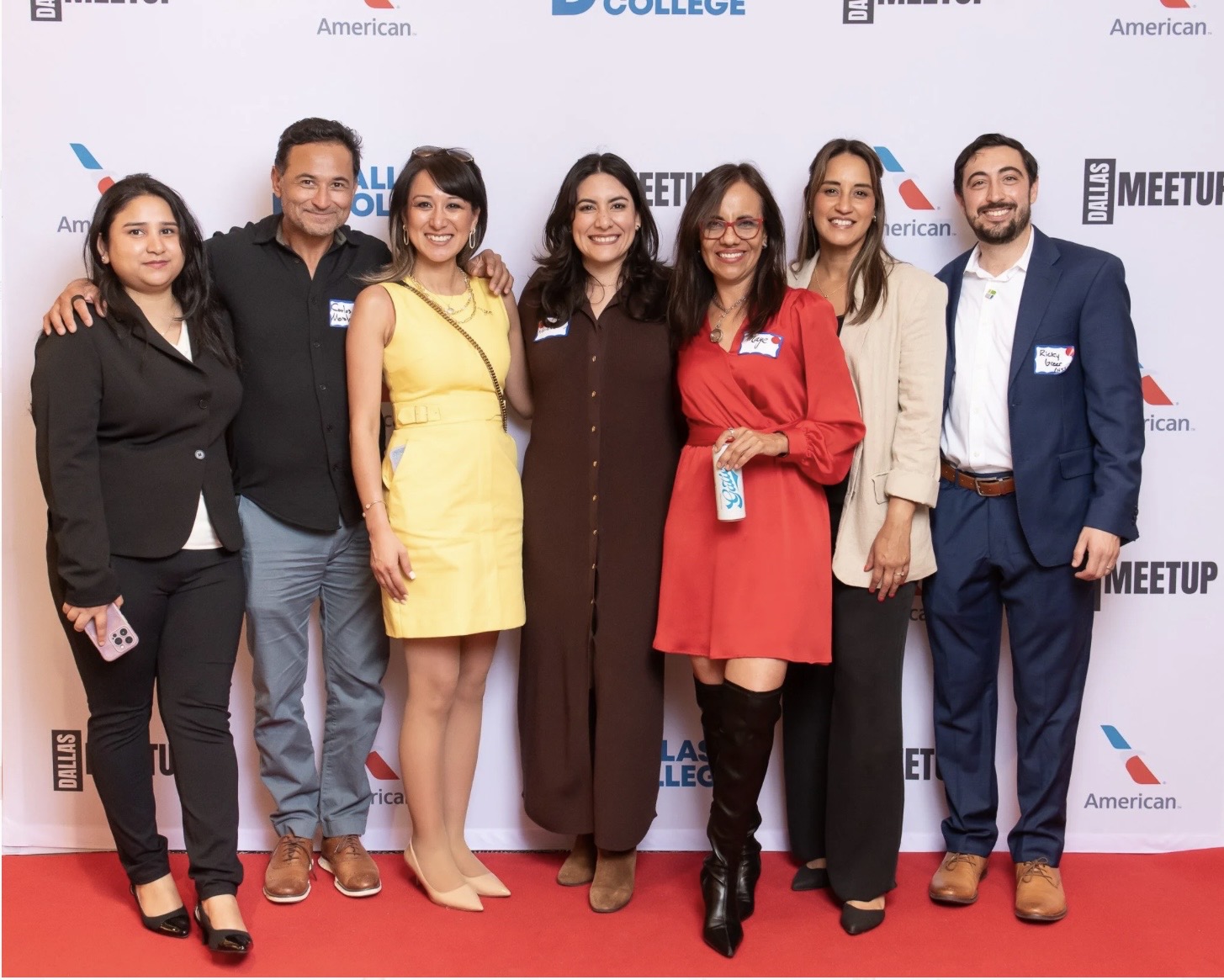 Group of seven people standing on a red carpet in front of a backdrop, smiling for the photo.