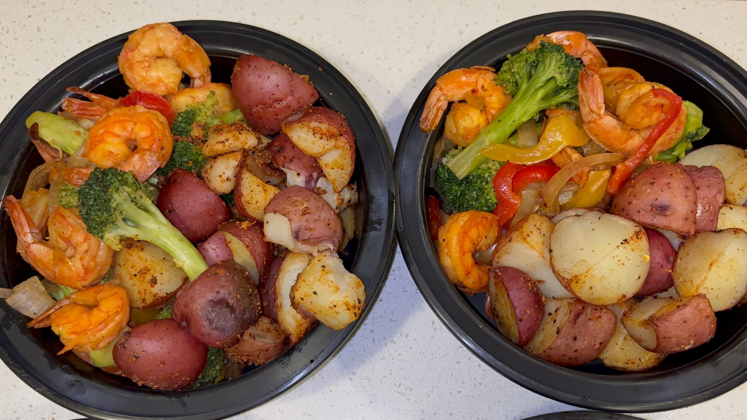 Two black bowls filled with cooked vegetables and potatoes, placed on a white surface.