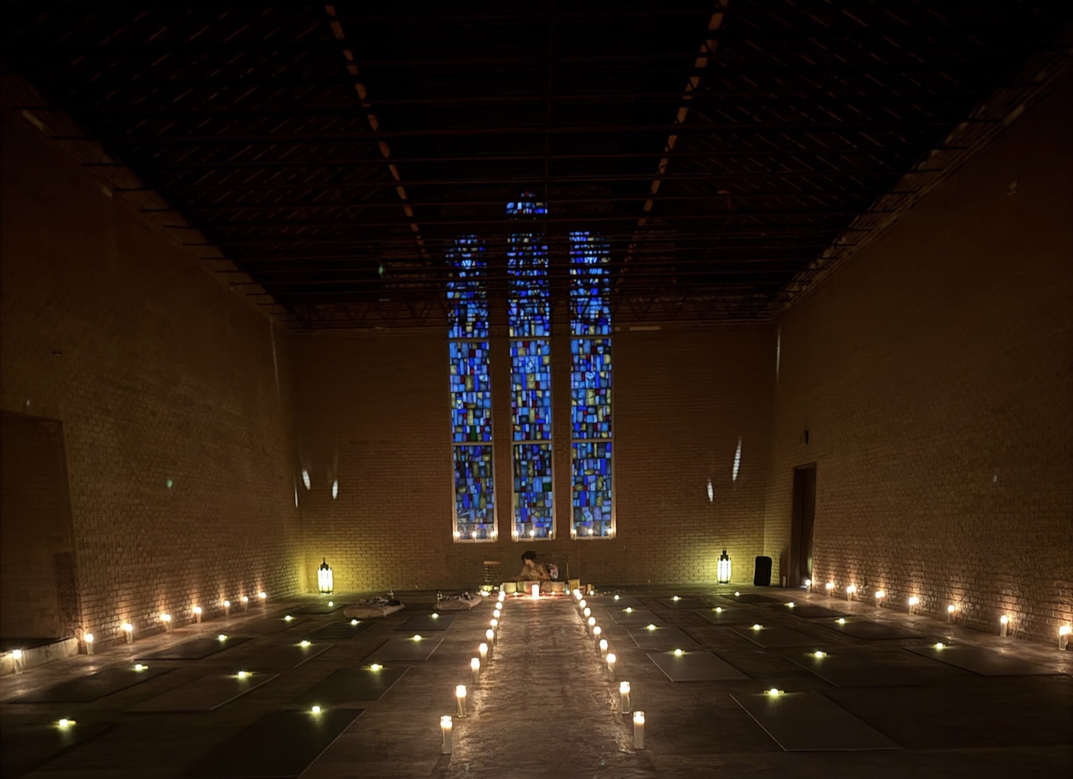 Interior of a church with a large stained glass window, candles, and dim lighting, creating a serene atmosphere.