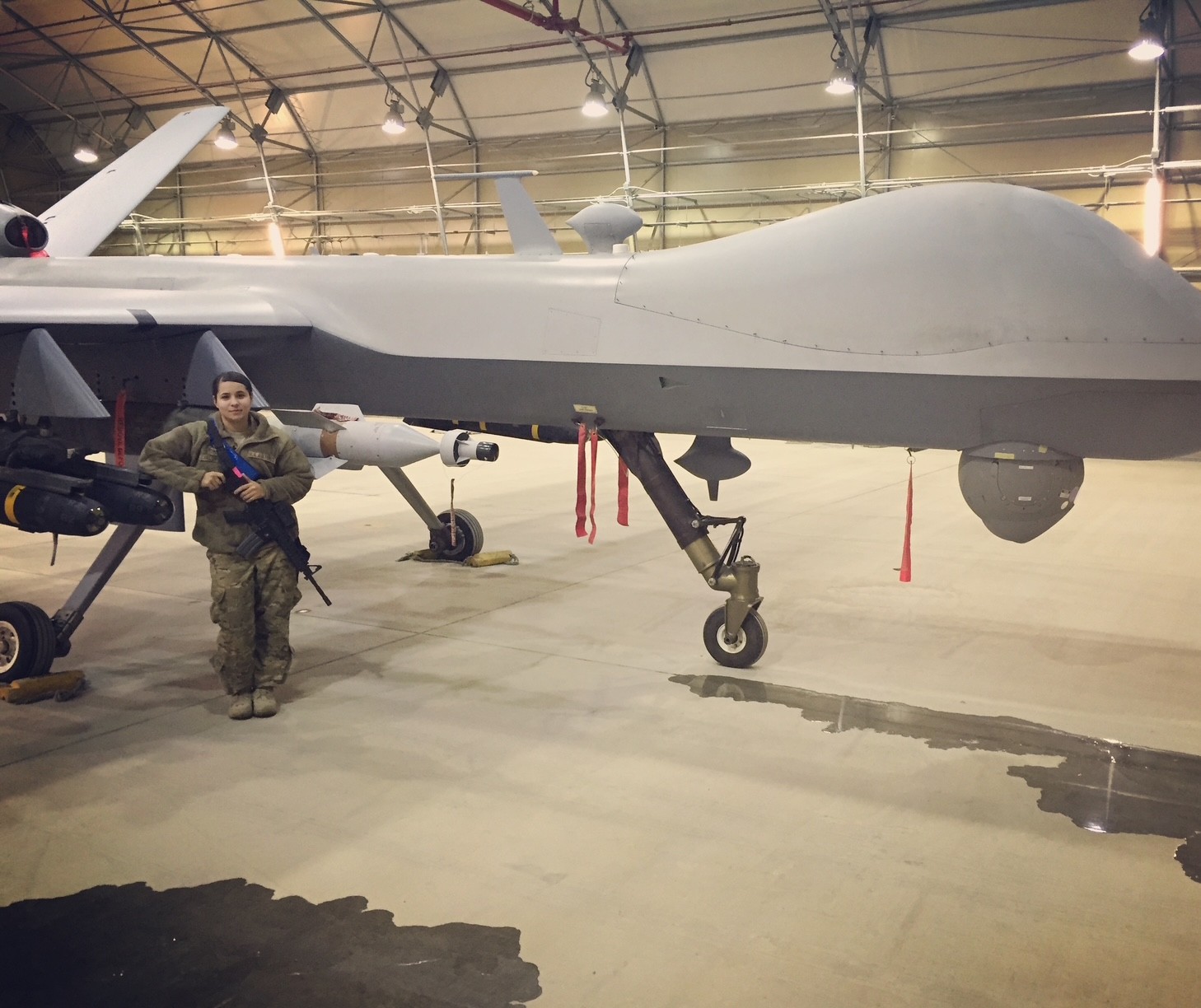 Person in military uniform standing next to a large unmanned aircraft inside a hangar.
