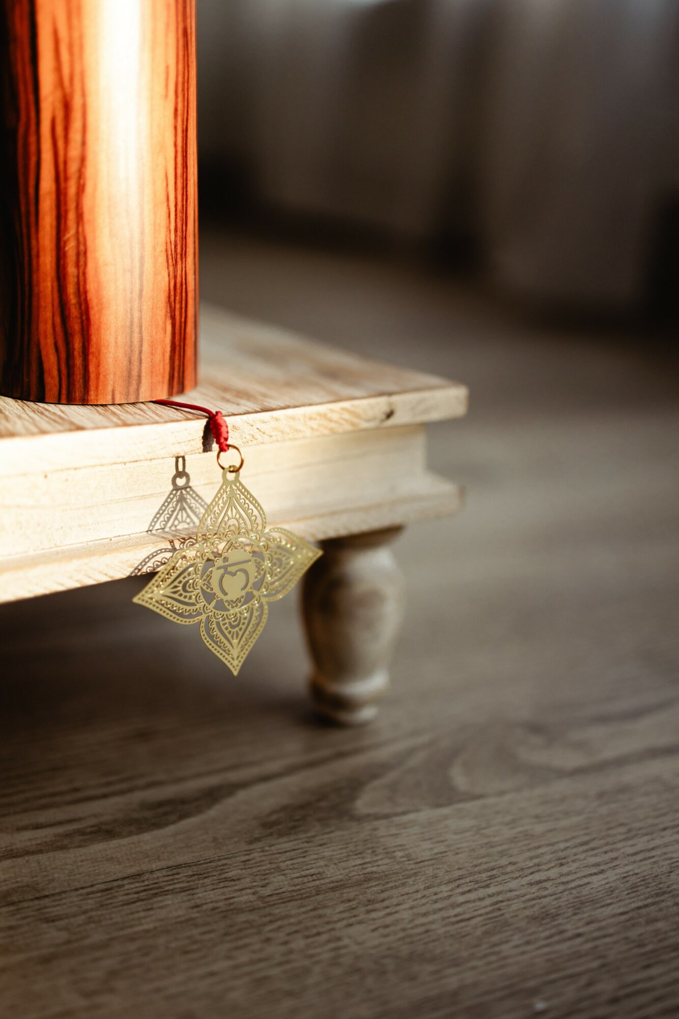 Decorative gold ornament hanging from a red string on a wooden table leg, with a blurred background.