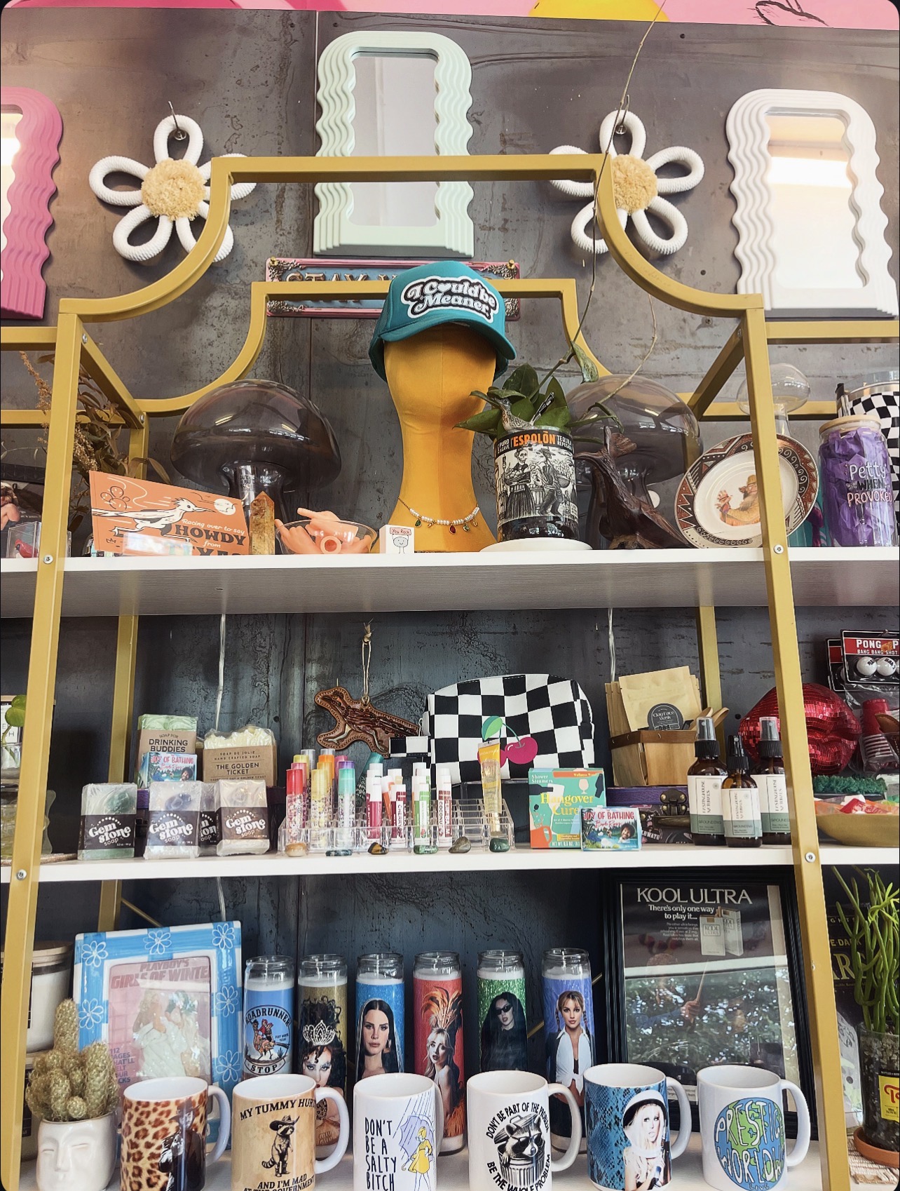 Display shelf with various products, including mugs, bottles, and decorative items, against a colorful background with a gold frame.