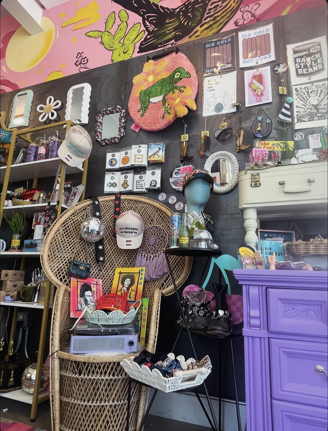 Display of colorful home decor items, including a wicker chair, framed pictures, and decorative objects on a black wall.