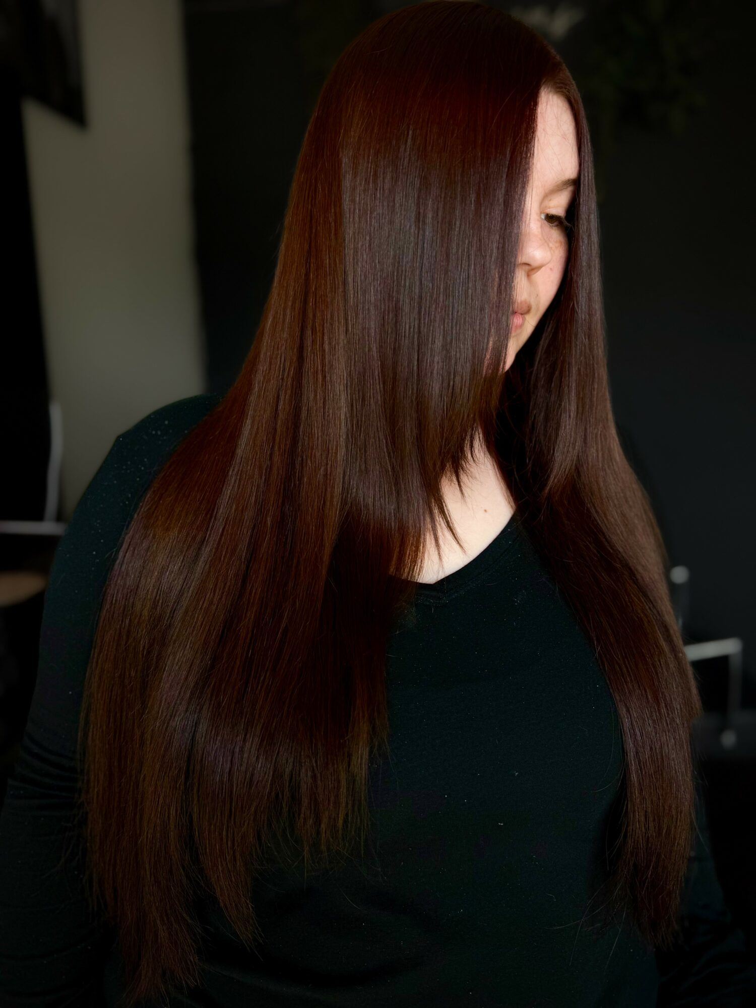 Side view of a woman with long, straight, reddish-brown hair wearing a black top.