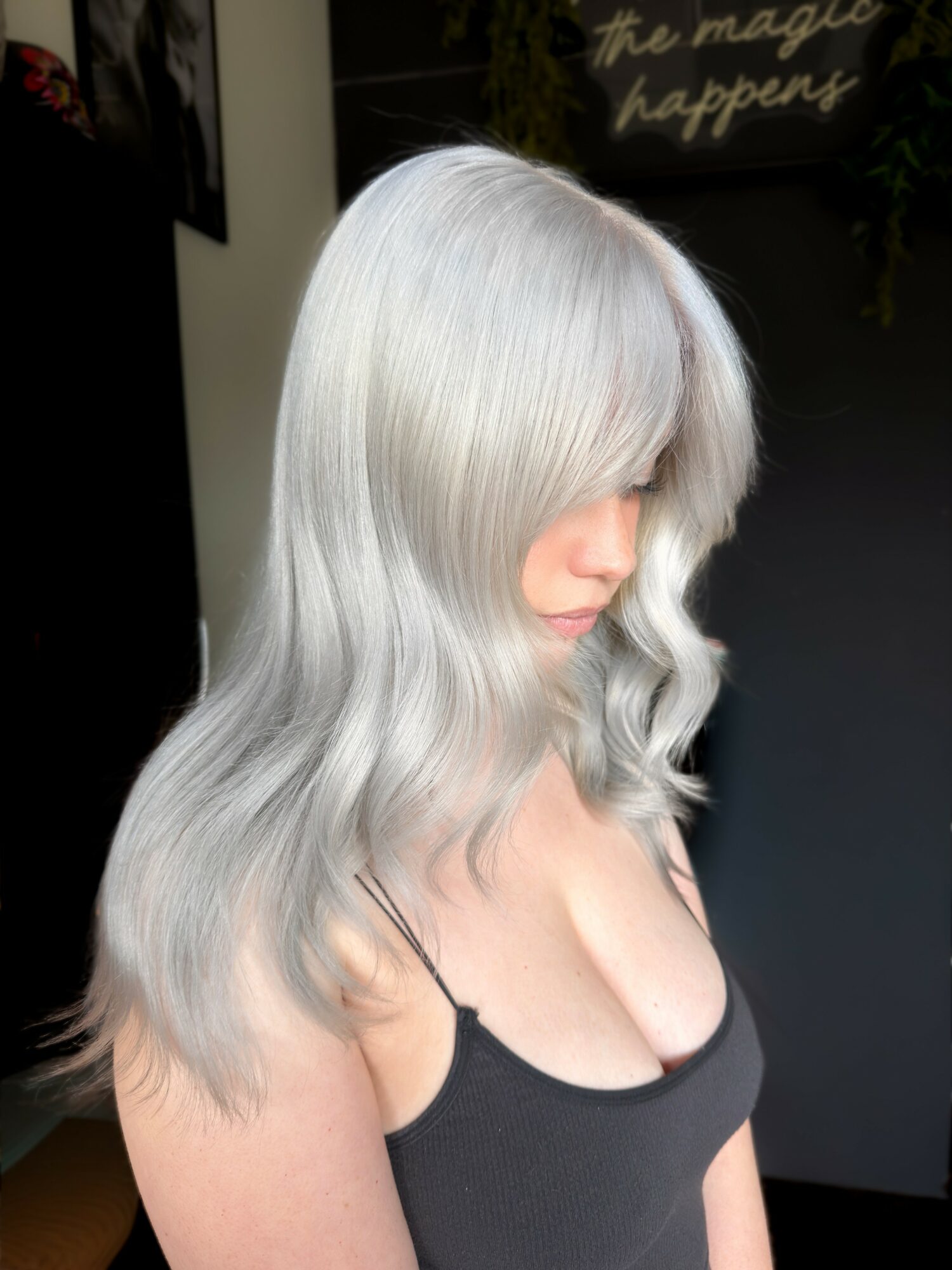 Woman with long, wavy, silver hair covering part of her face, wearing a black spaghetti strap top.
