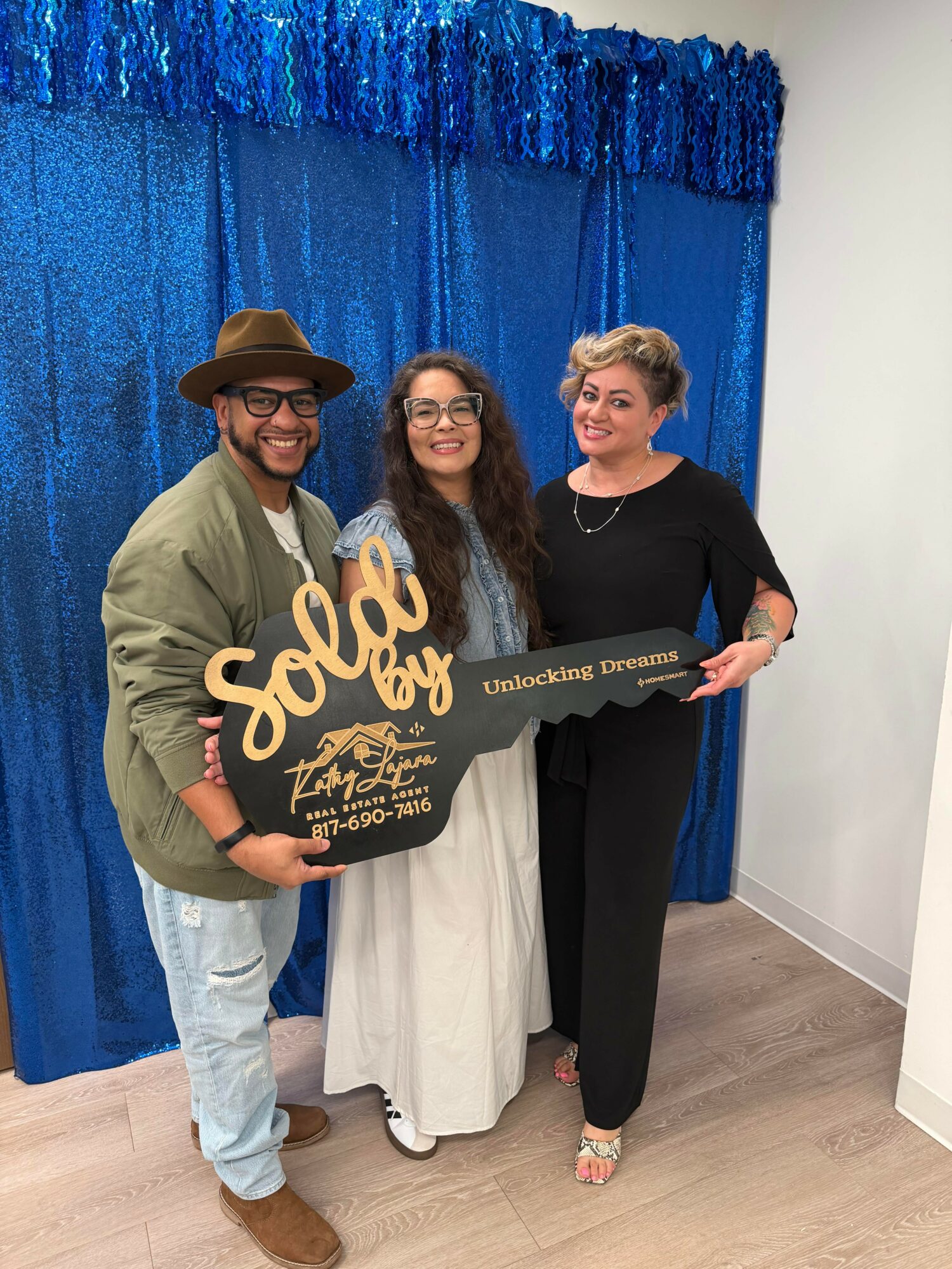 Three people standing in front of a blue curtain, holding a large sign that says