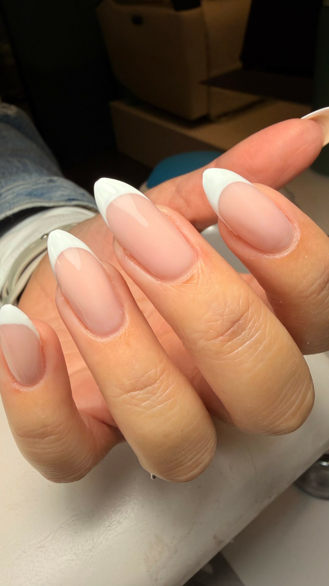 Close-up of a hand with manicured nails featuring white tips and a natural base, resting on a surface.