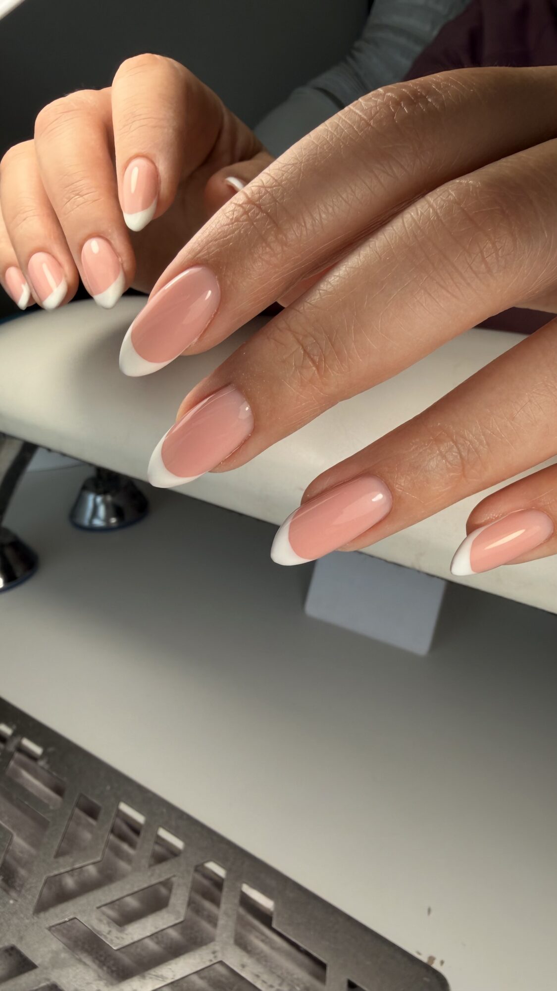 Close-up of well-manicured hands with light pink nails resting on a white surface.