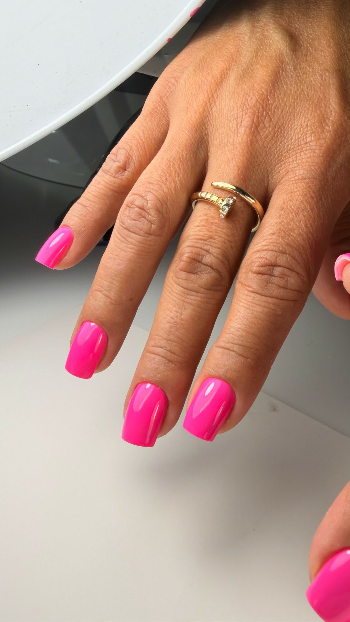 Hand with pink nail polish, wearing two rings, resting on a white surface.
