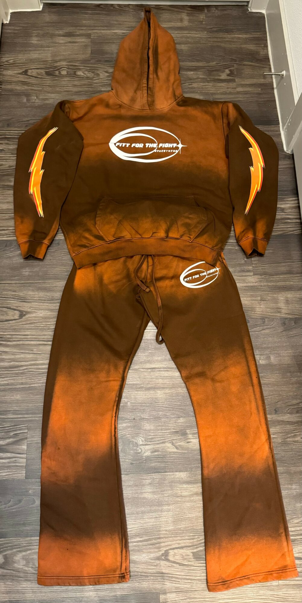 Brown and black tracksuit with white logo, laid flat on a wooden floor.