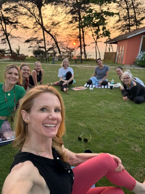 Group of people sitting on grass during sunset, smiling and enjoying outdoor gathering.