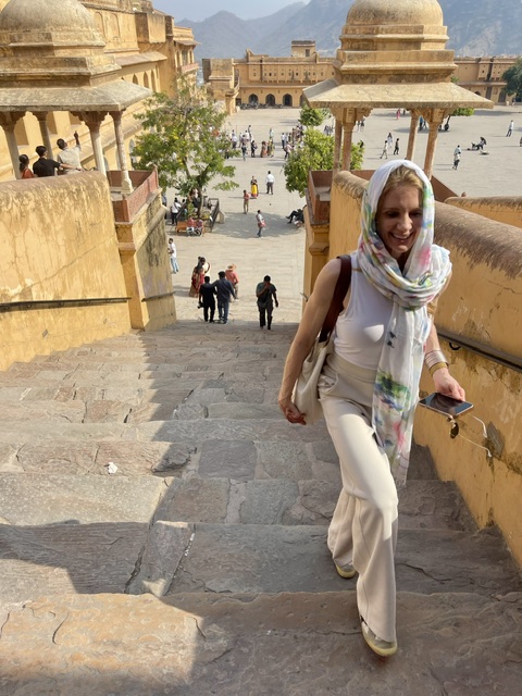 Woman with a scarf walking up stone stairs at historic site with buildings and people in background.