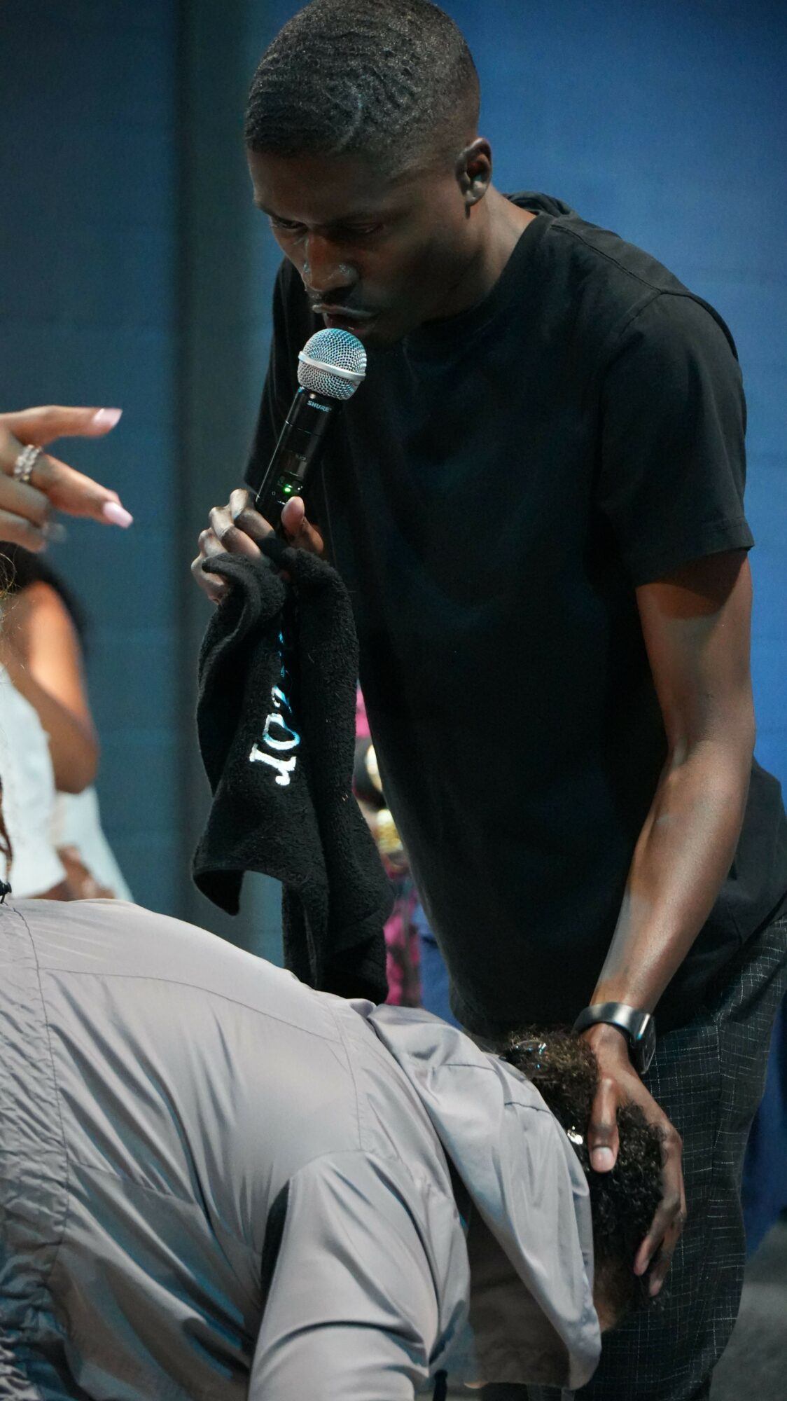 Person speaking into a microphone held by another person, with a dark background.